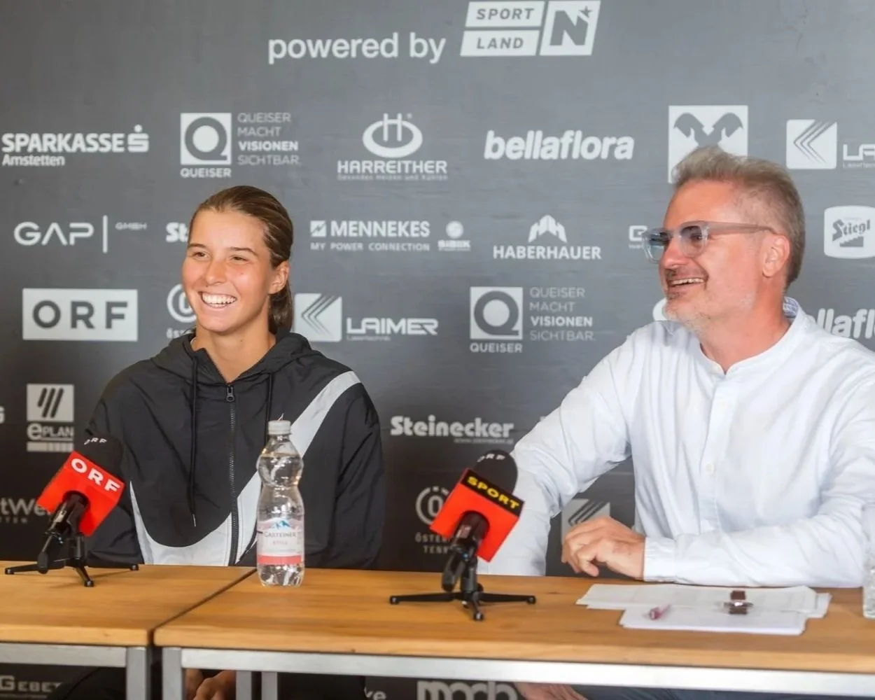 Lilli Tagger und LADIES OPEN Amstetten-Pressechef Mathias Sollböck bei der Pressekonferenz 2025. Tagger lächelt, Sollböck antwortet auf eine Journalistenfrage. Es gibt Mikrofone mit ORF-SPORT-LOGO auf dem Tisch.