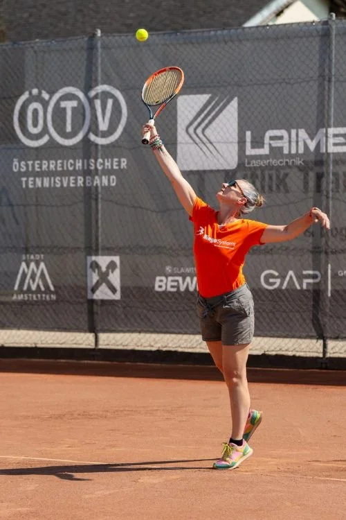 Mädchen beim Tennis auf einem roten Sandplatz, spielt den Ball mit einem Tennisschläger, wearing sunglasses und einem orange T-Shirt.