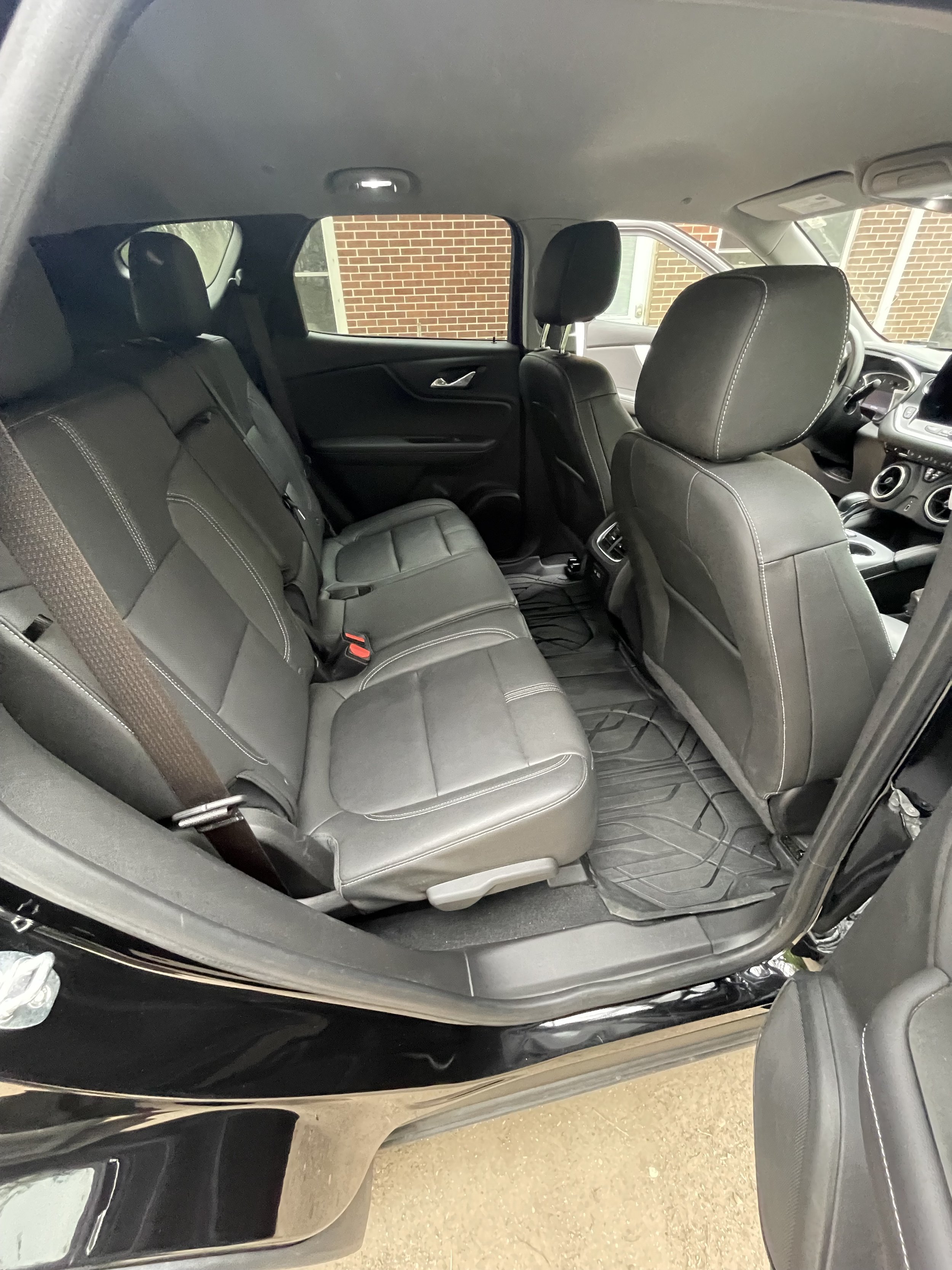 The interior of a black SUV showing the back seat, front seats, and dashboard with a view of the outside brick wall through the window.