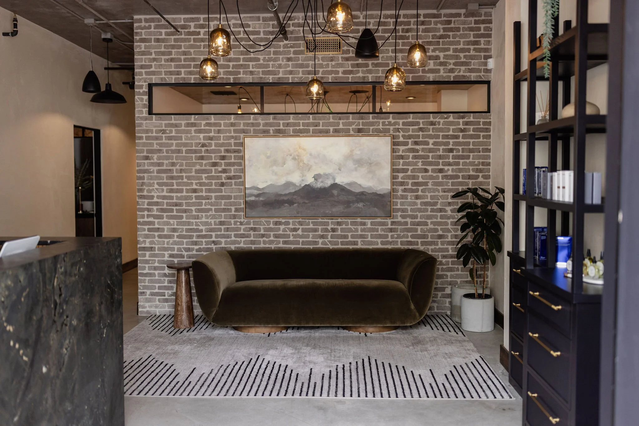 Modern living room with exposed brick wall, abstract painting, and hanging light fixtures.