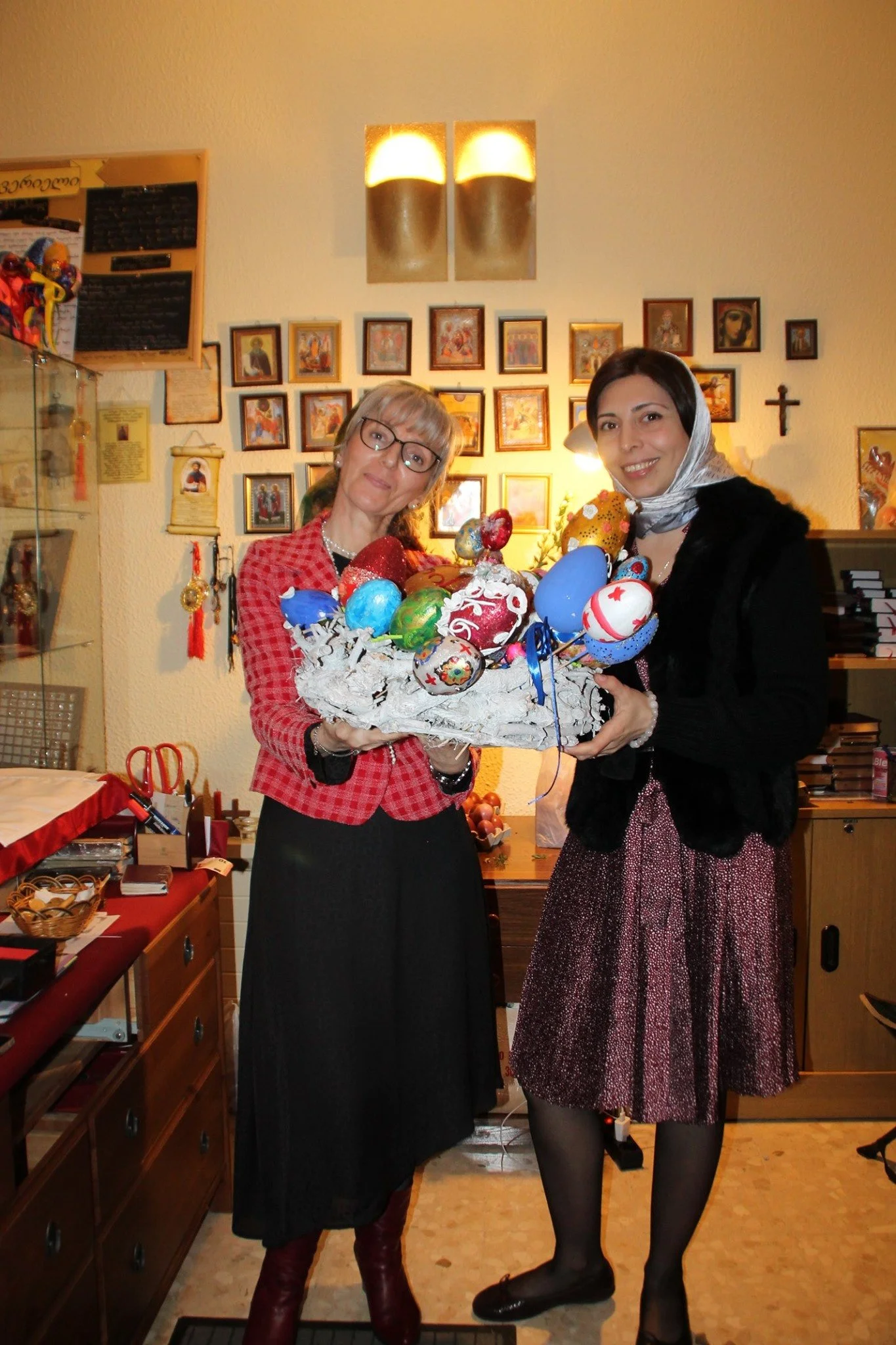 Dos mujeres en una celebración de Pascua, una sostiene una canasta con huevos decorados y la otra sonriendo.