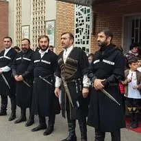 Un grupo de hombres vestidos con trajes tradicionales, algunos con espadas, de pie frente a un edificio, posiblemente participando en una ceremonia o evento cultural.
