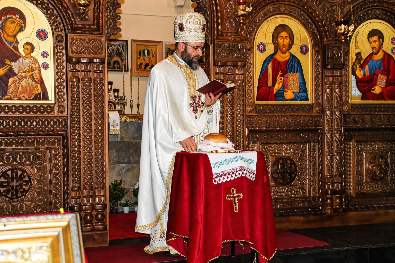 Un sacerdote ortodoxo vestido con vestimenta blanca y un mitra decorada con cruces, realizando una ceremonia en una iglesia con iconos religiosos en el fondo, frente a una mesa con un pan y un tapiz de bordado.