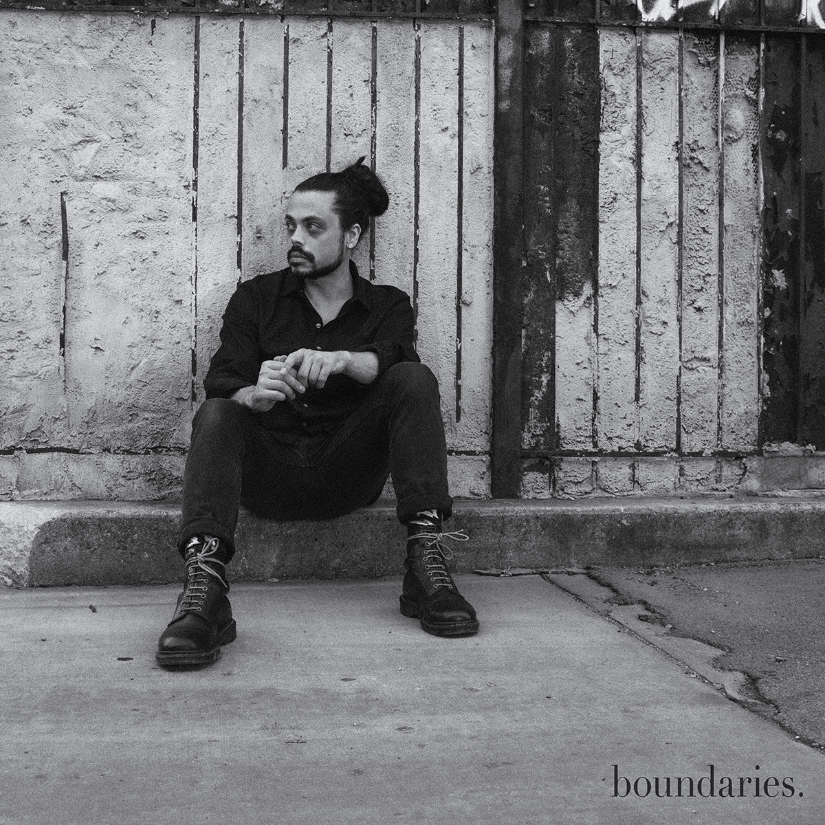 saint Ripley boundaries album cover a man with long hair tied up in a bun sitting in an alley against a building looking to his side wearing doc marten boots and an all black outfit