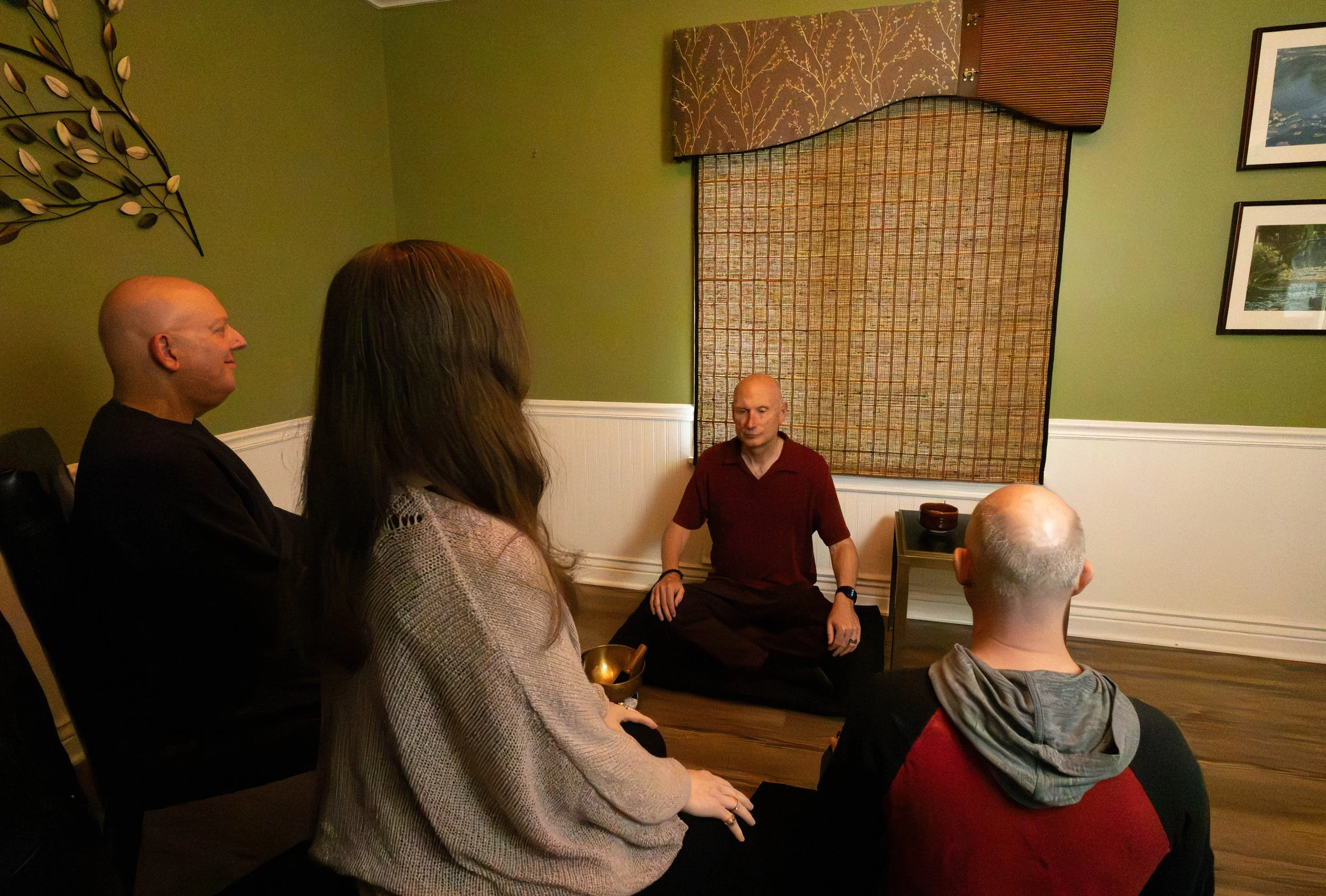 Image of John leading a group meditation session with three people shown seated facing John.