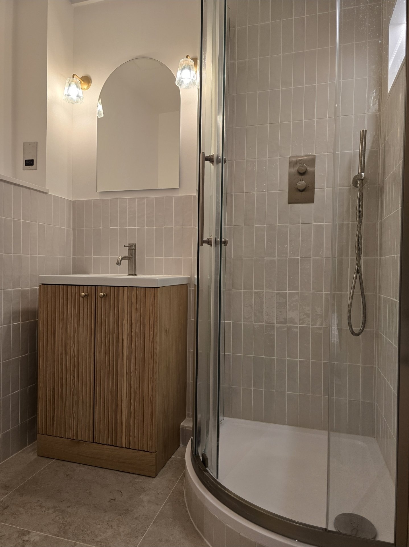 Bathroom with a vanity, mirror, wall-mounted lights, and a shower with glass door and handheld showerhead.