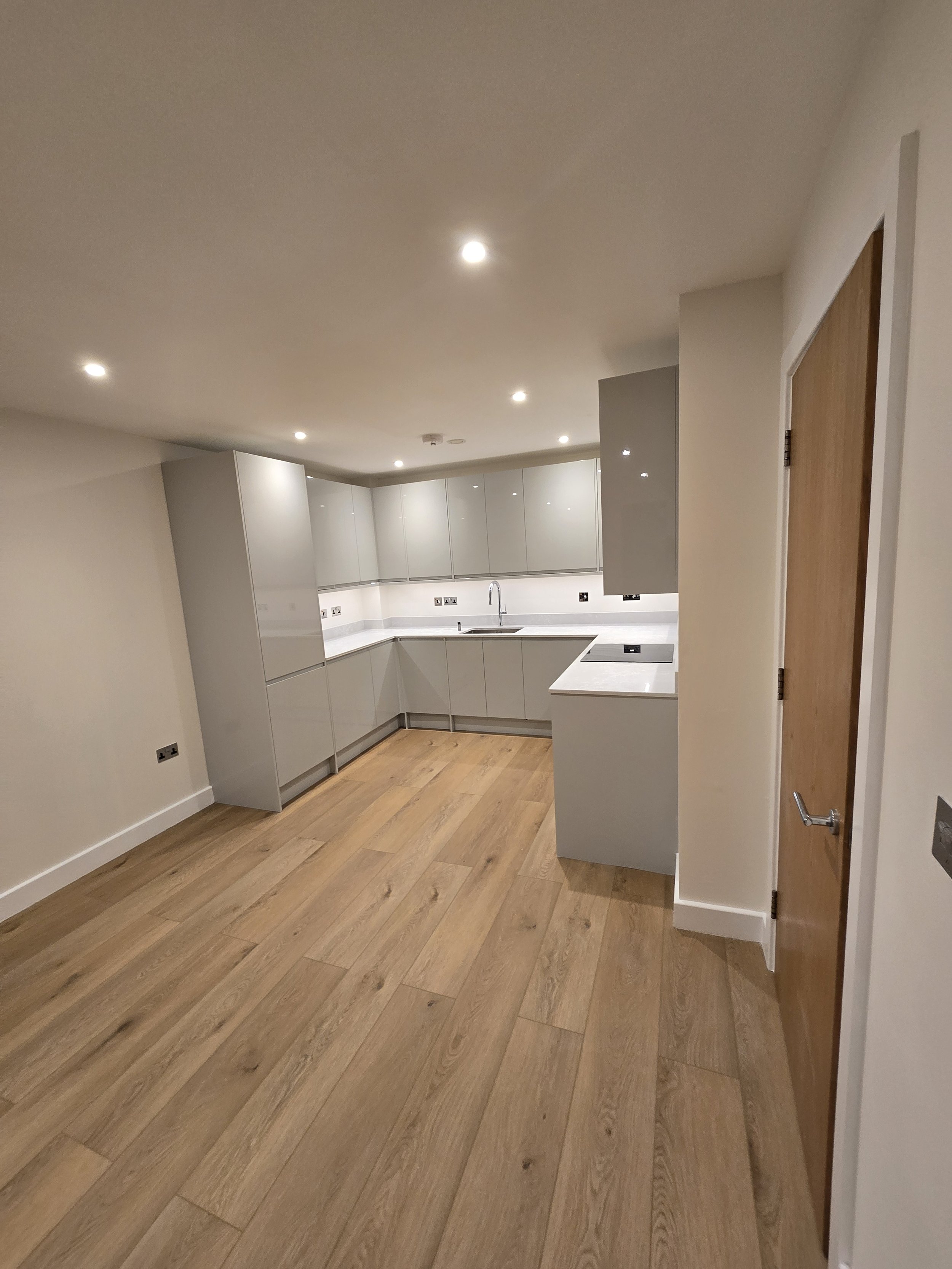 Modern kitchen with white cabinets, wooden flooring, and neutral-colored walls. Recessed ceiling lights illuminate the space.
