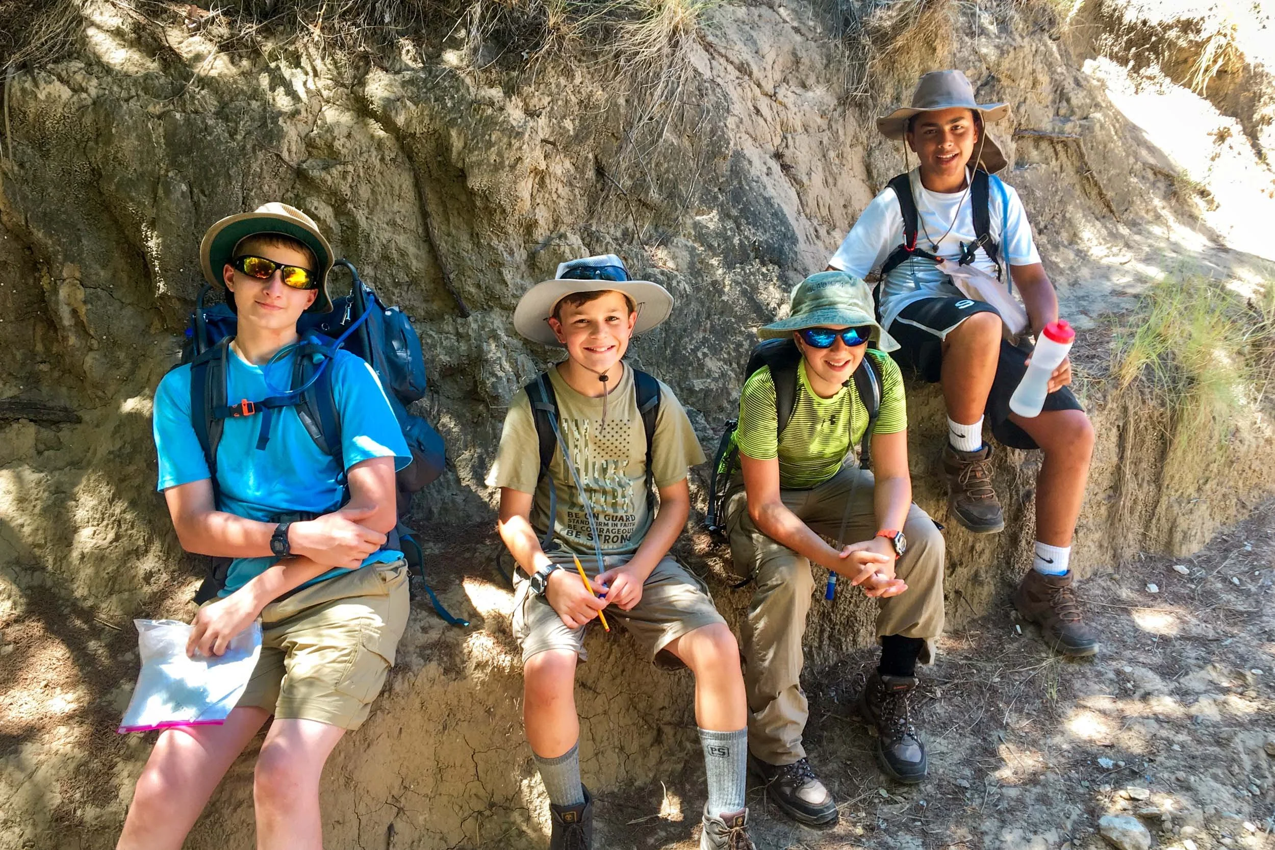 Campers in hiking gear resting on a rocky cliff.