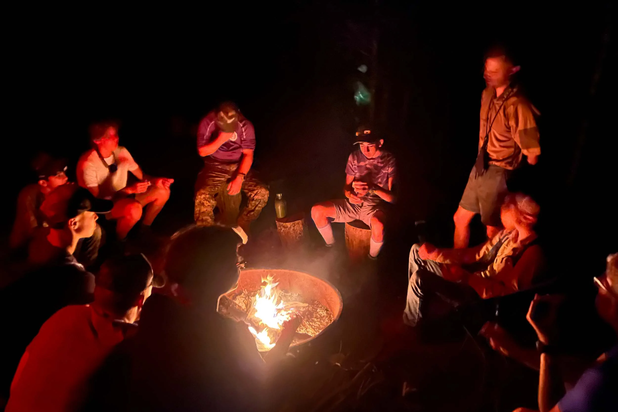 Group of people sitting around a campfire at night.