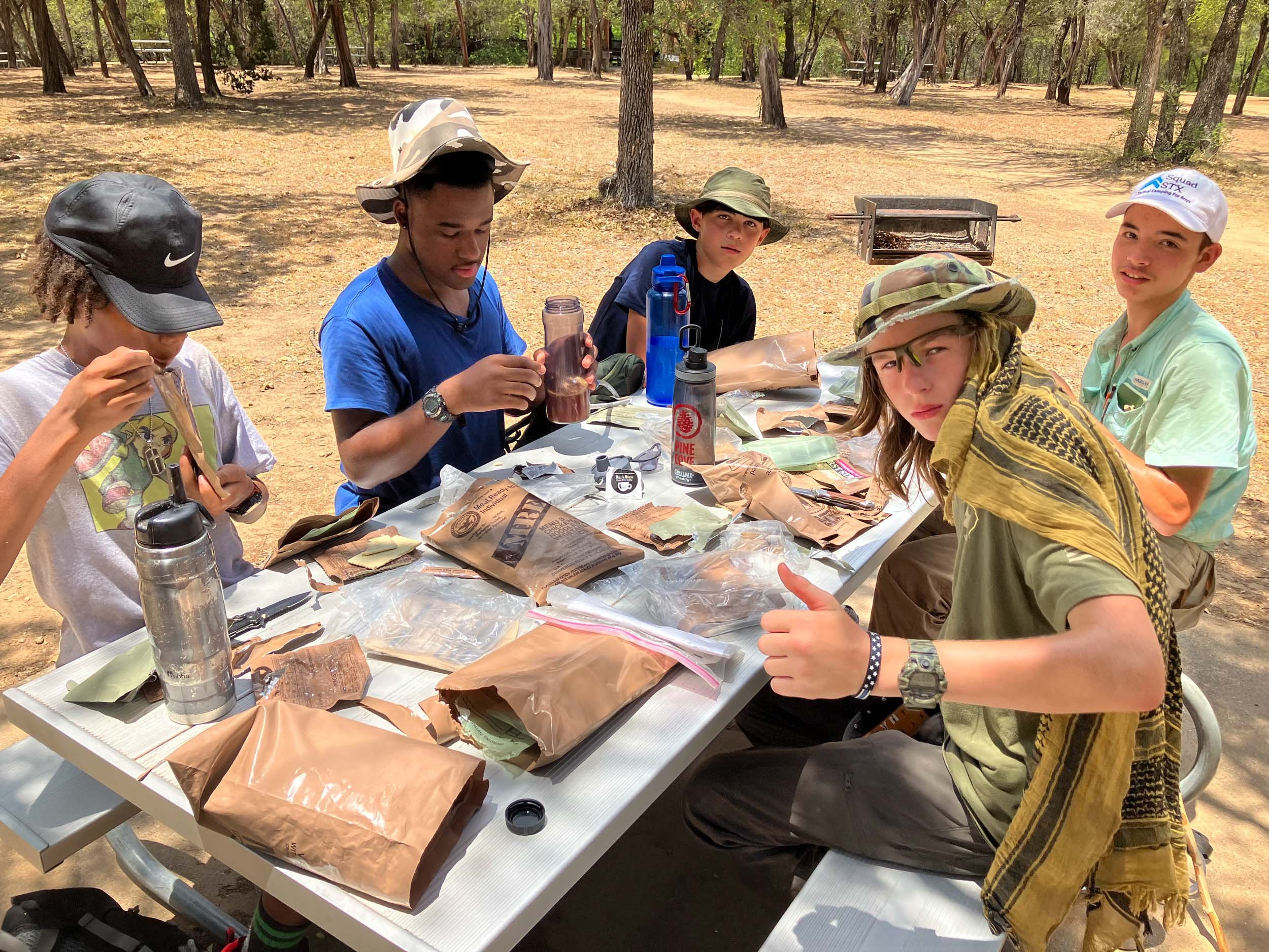 Campers sitting outdoors eating MREs as a snack.