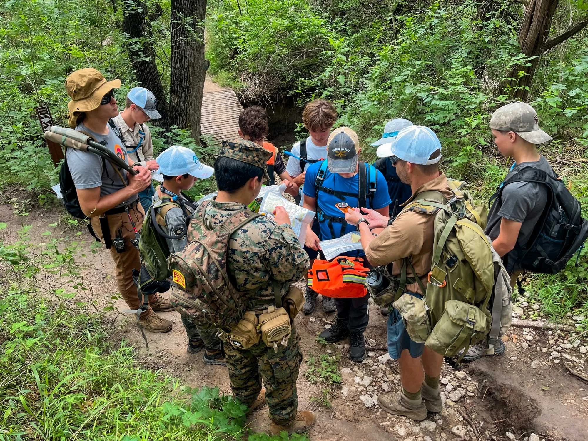 A group of campers and staff on a nature trail, gathered around studying a map.