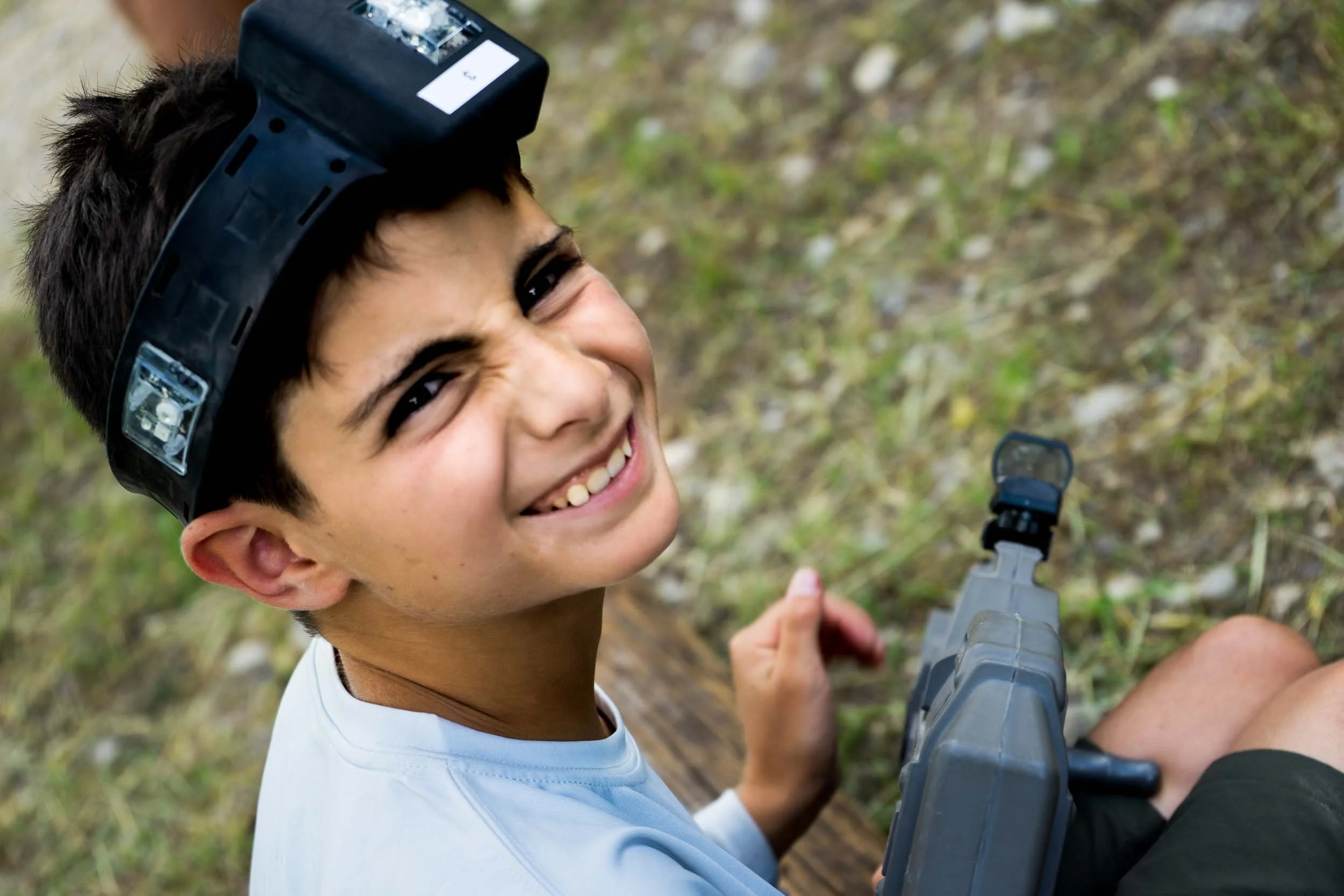 A young boy smiling outdoors while holding a laser tag gun.
