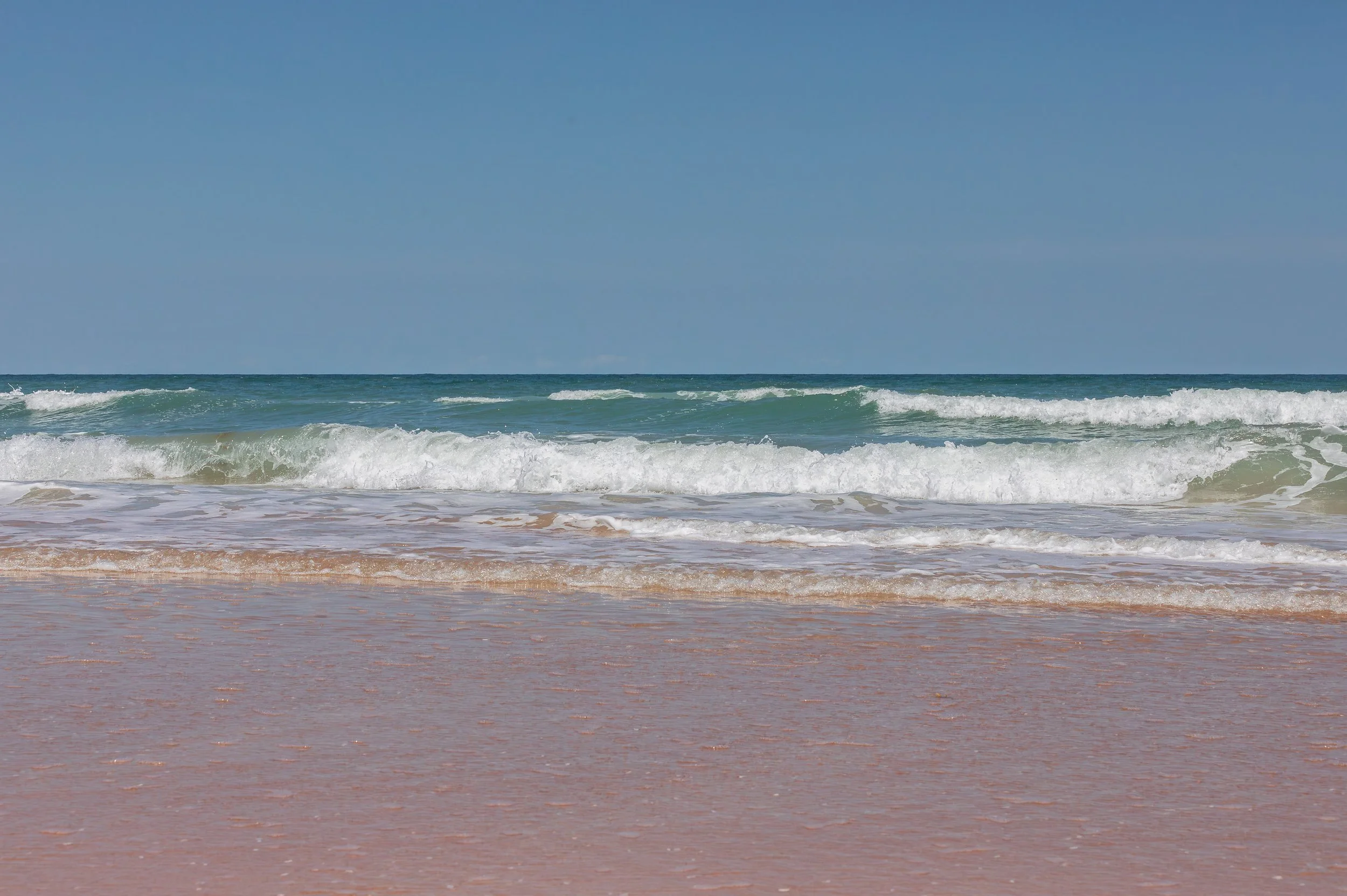 Photo of the ocean with blue sky, waves crashing onto the sandy beach. Ormond Beach Florida