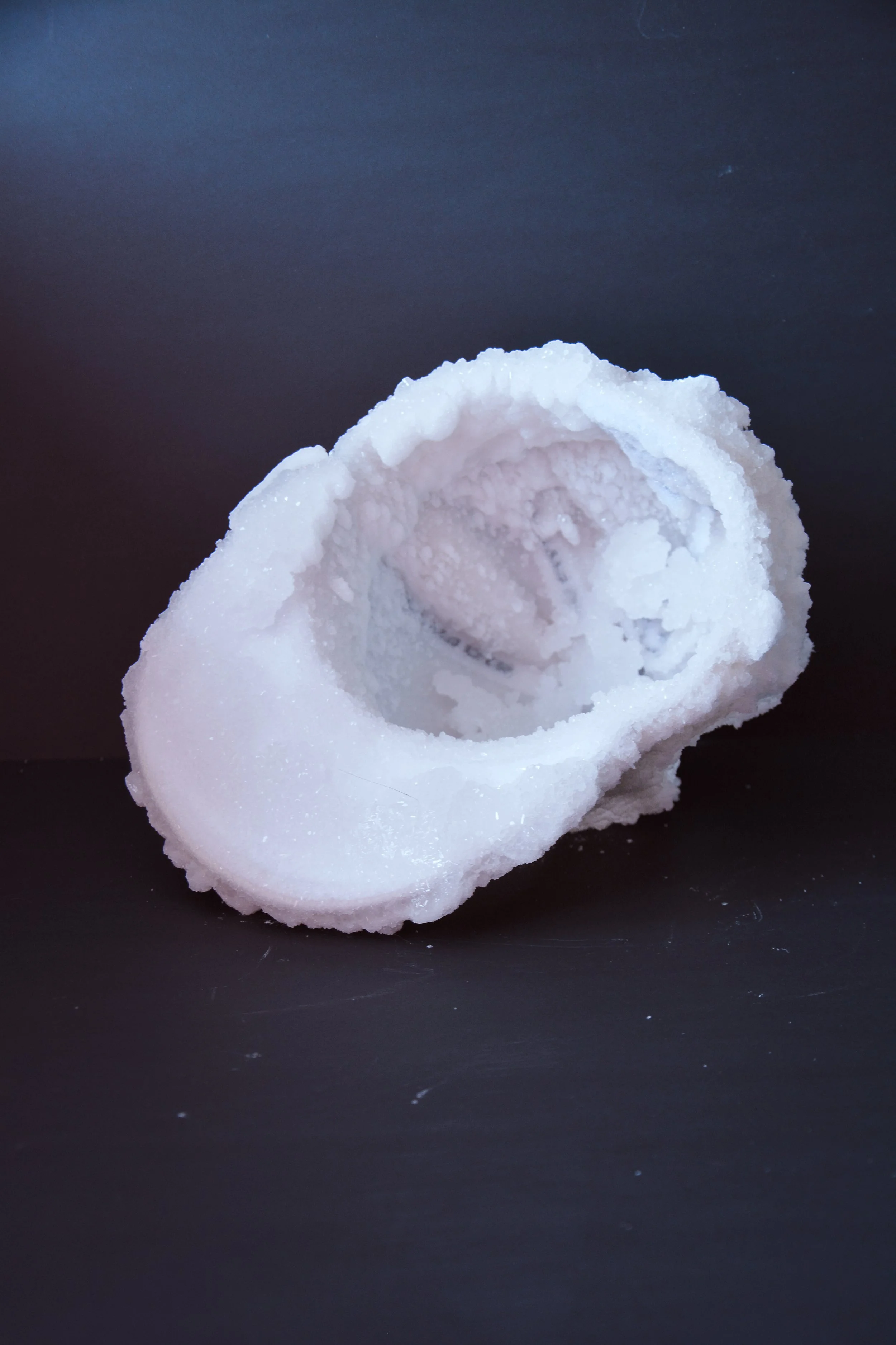 Close-up of a salt shaker with salt spilled around it, placed on a black surface.
