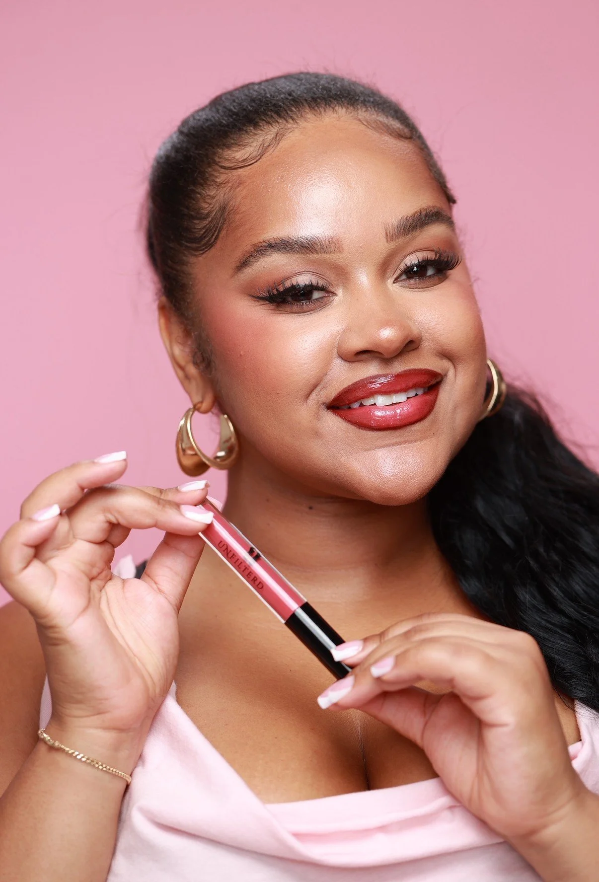 Woman, smiling, holding tube of Plush Lip Gloss