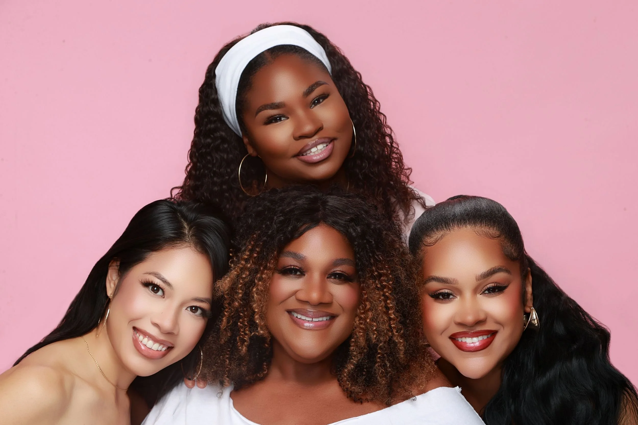 A group of diverse women smiling together against a pink background.