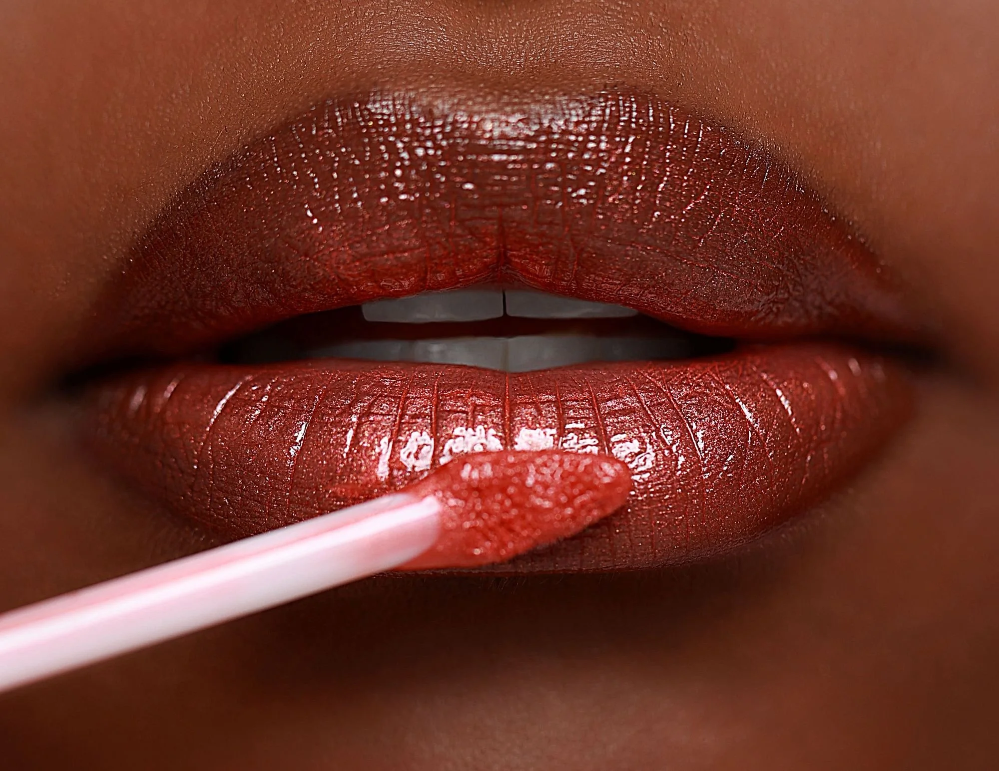 Close-up of lips with red lipstick applying lip gloss with a pink and white striped applicator.