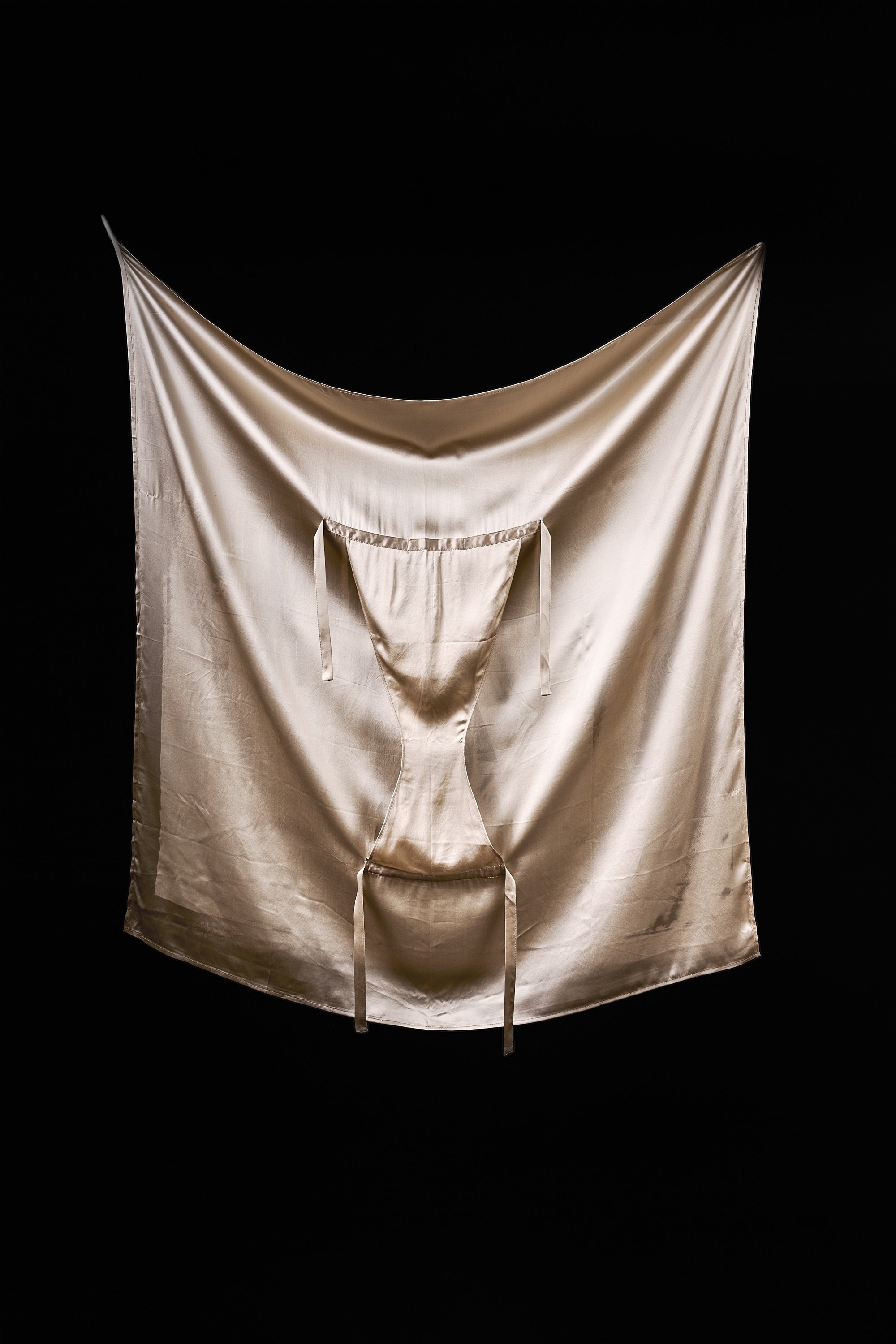 A satin sheet or fabric hanging against a black background, with a draped appearance and a slit in the center.