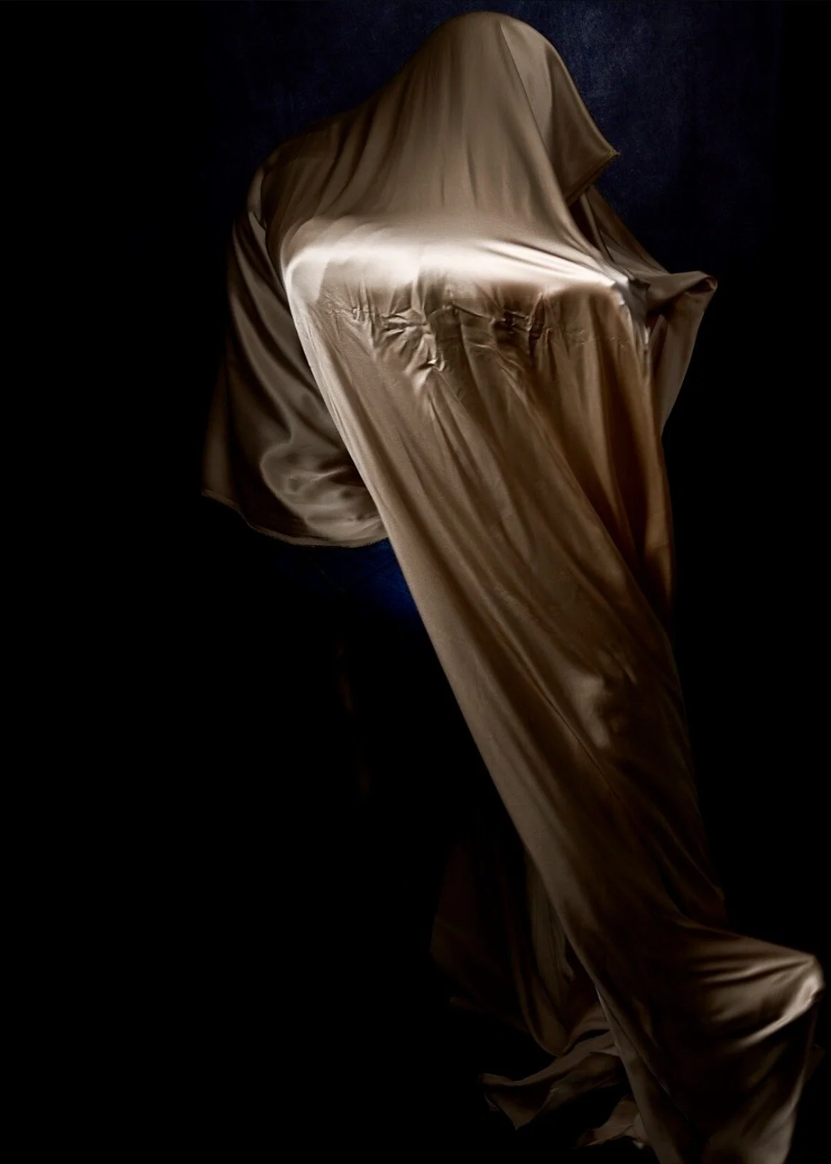 A chair covered with shiny beige fabric in a dark environment with a black background.