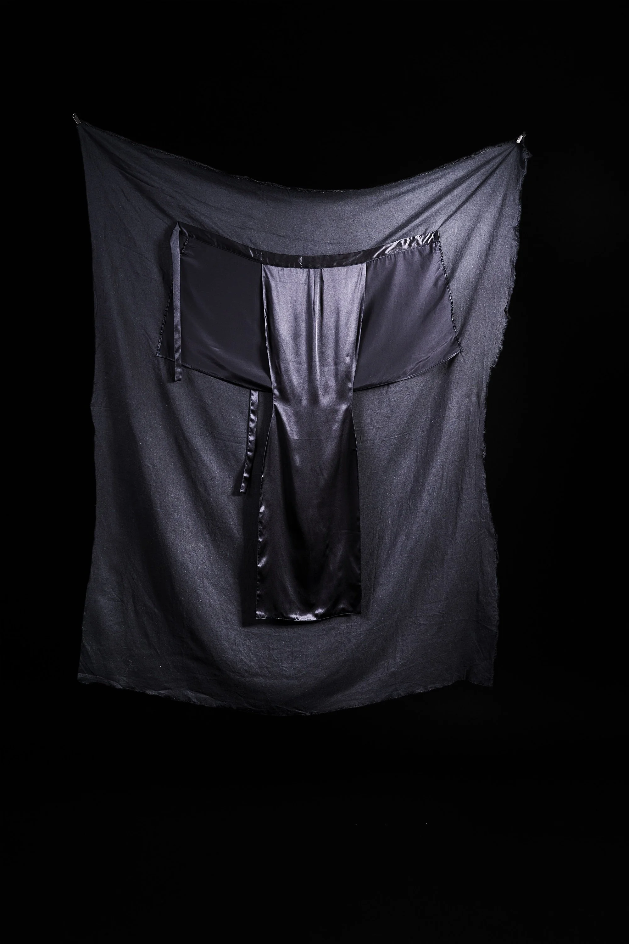 A black silky dress hanging on a black background.