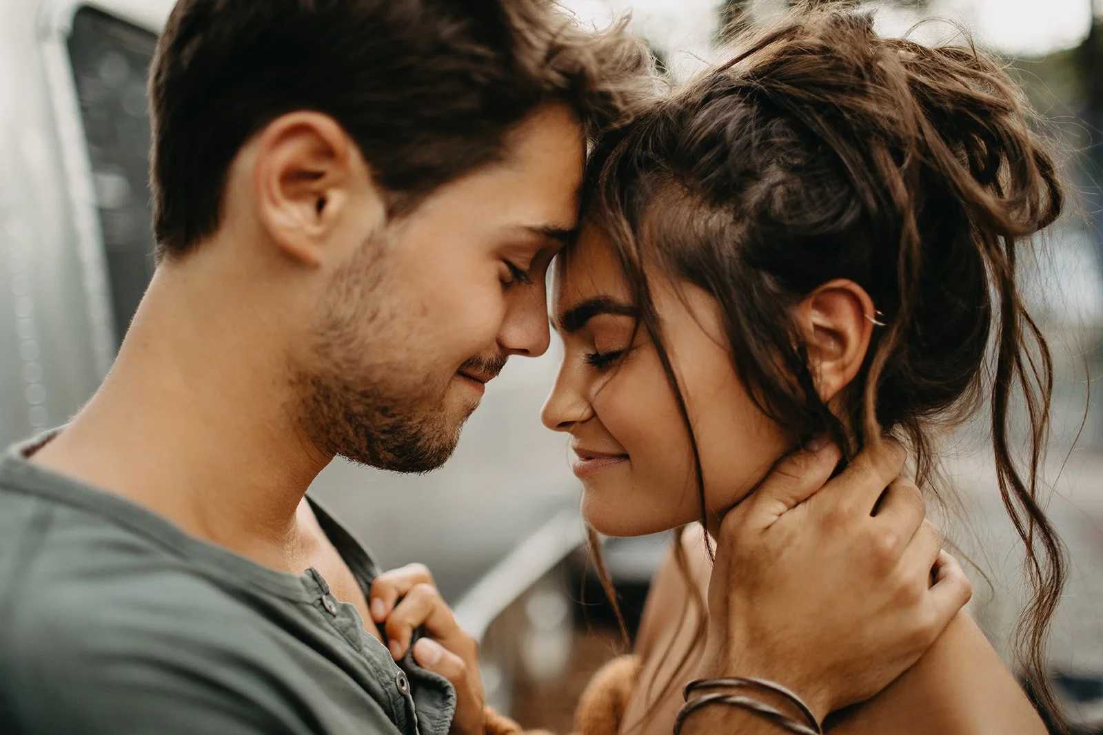 A young man and woman are touching foreheads and smiling with their eyes closed, showing affection and intimacy.