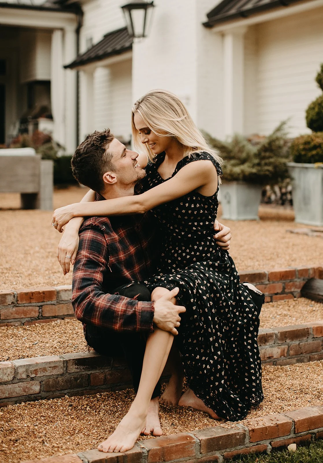 A man and woman sitting on brick steps outdoors, embracing and smiling at each other.