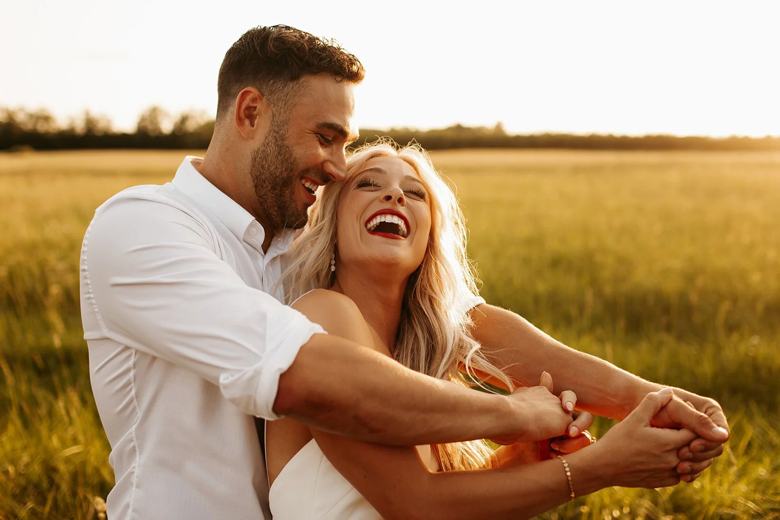 A couple laughing and embracing in a field during sunset, outdoor scene with bright sunlight.
