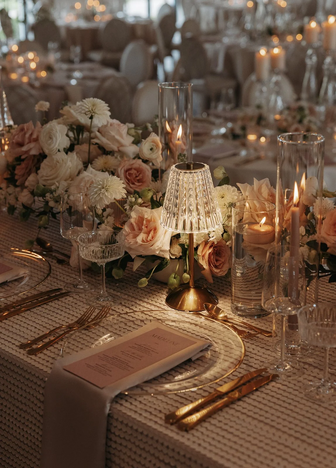 Elegant dining table setup with a floral centerpiece, candles, and gold cutlery at an event or wedding reception.