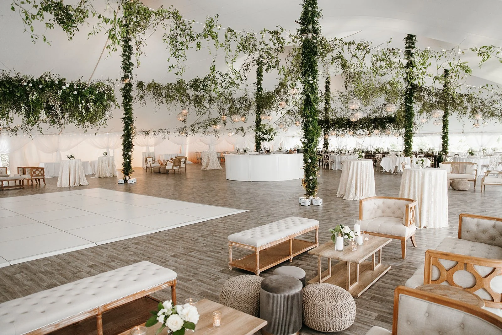 Elegant wedding reception venue with white drapery, floral arrangements, and vintage-inspired furniture, including sofas and ottomans, with a dance floor and a bar area.