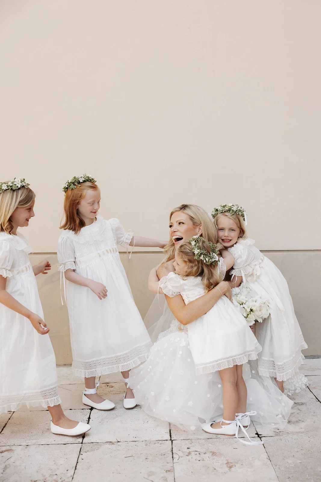 A woman surrounded by five young girls in white dresses and floral headbands, appearing to be at a celebration or special occasion.