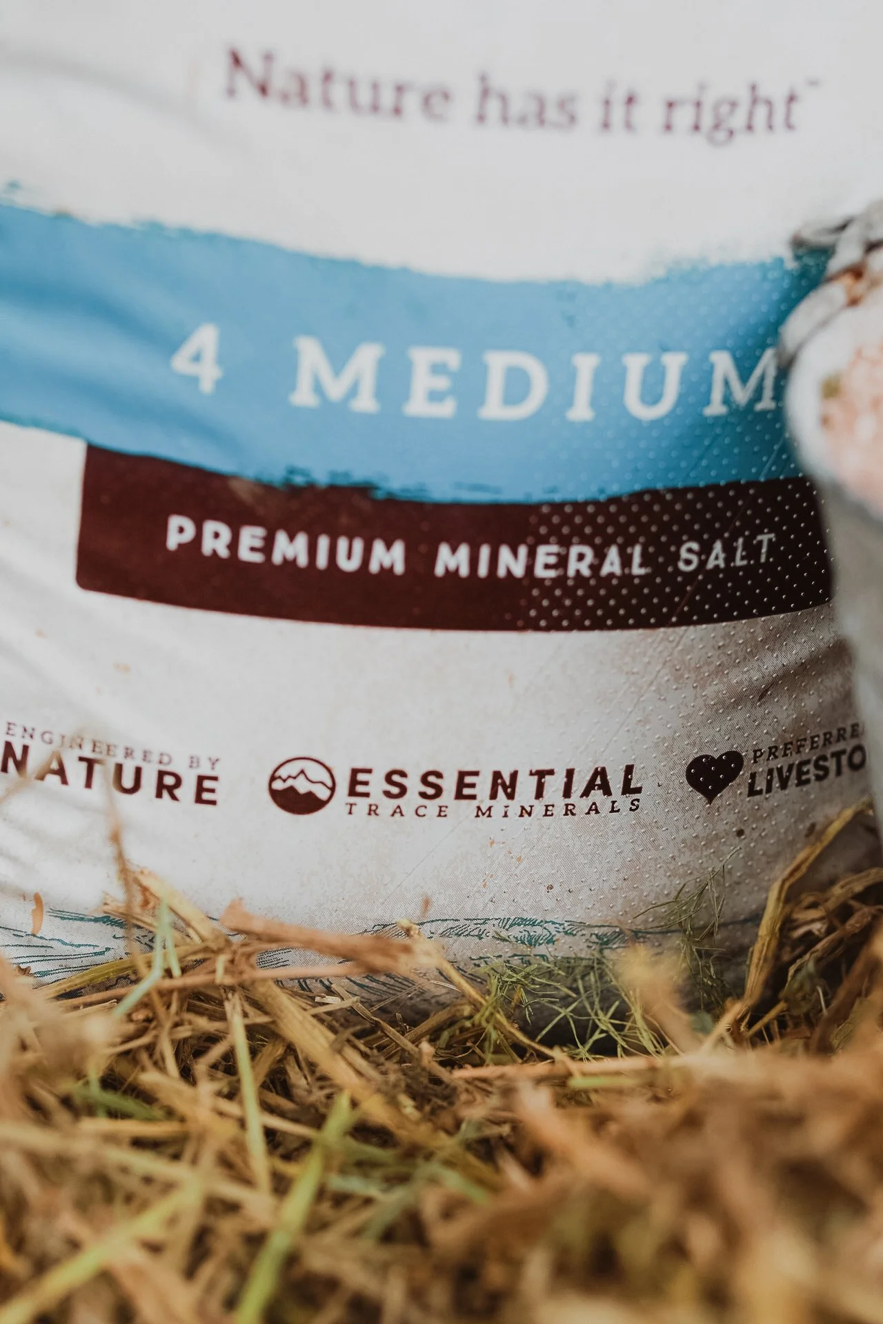 A close-up of a bag of premium mineral salt with the text '4 MEDIUM' and 'Nurture has it right' visible, surrounded by dried grass.