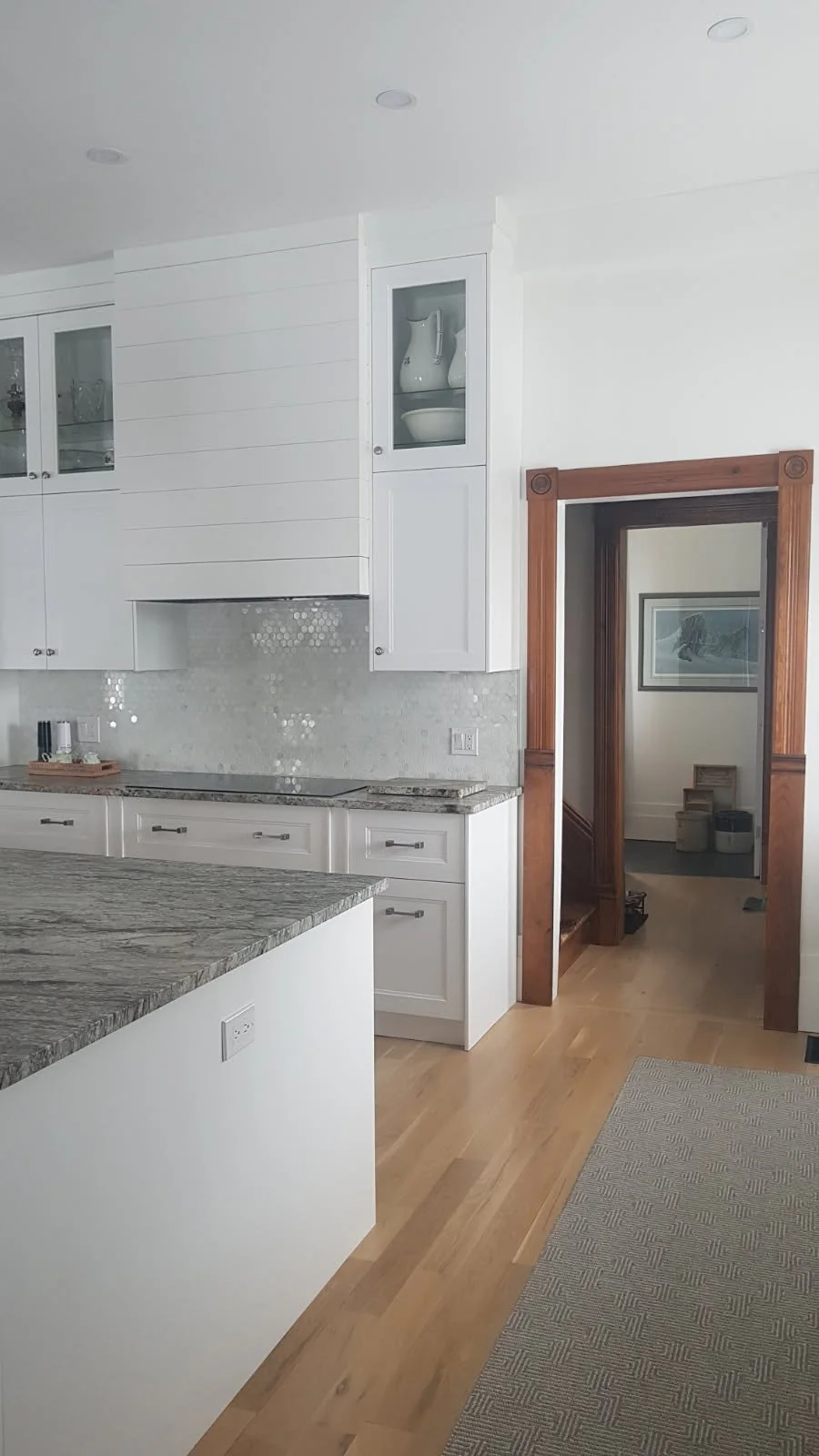 White cabinetry and a shiplap-style range hood sit alongside a wood-trimmed doorway for a simple mix of light and warm finishes.