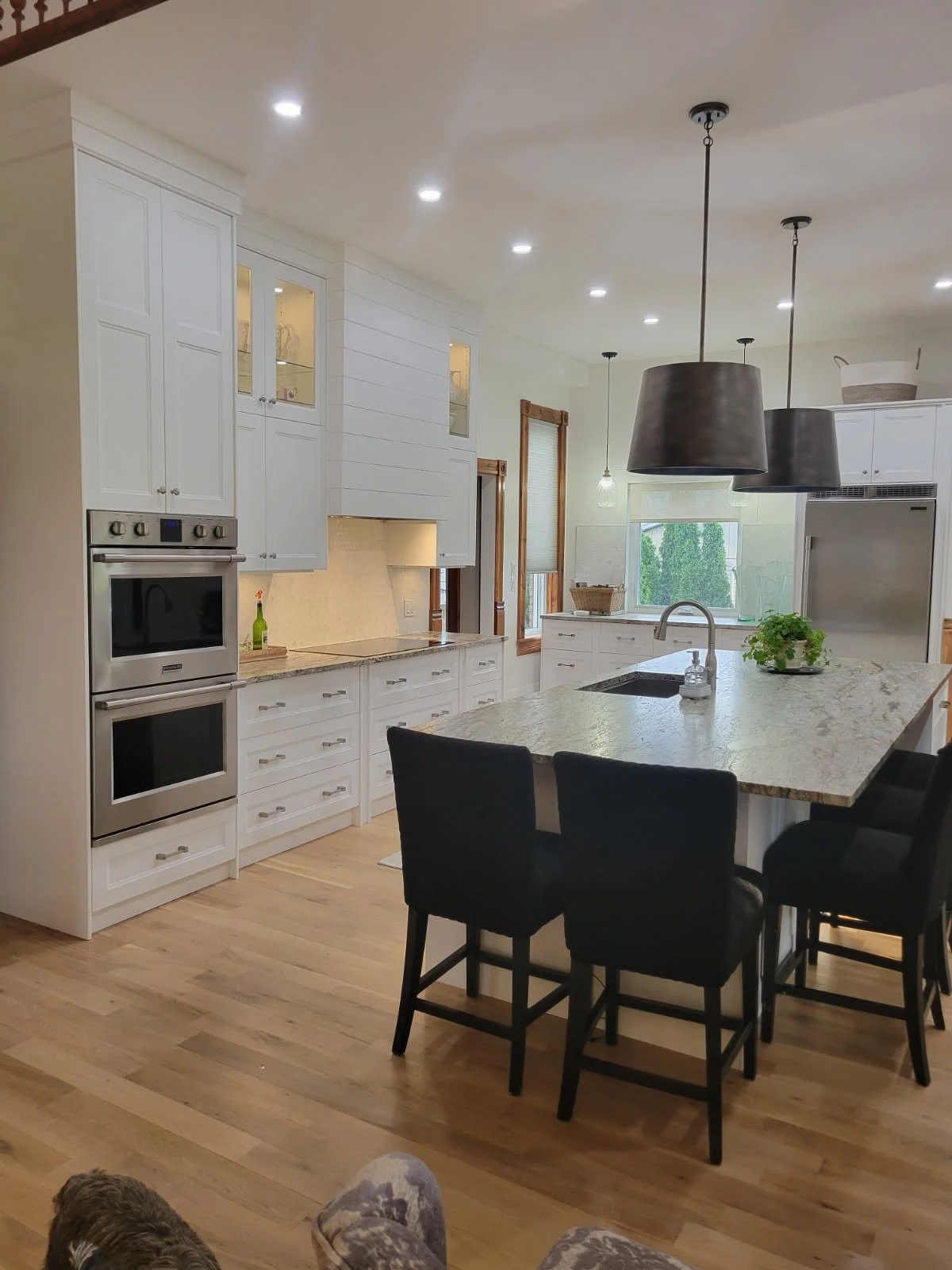 Glass-front cabinets and warm under-cabinet lighting soften the white cabinetry, while dark stools add contrast at the island.