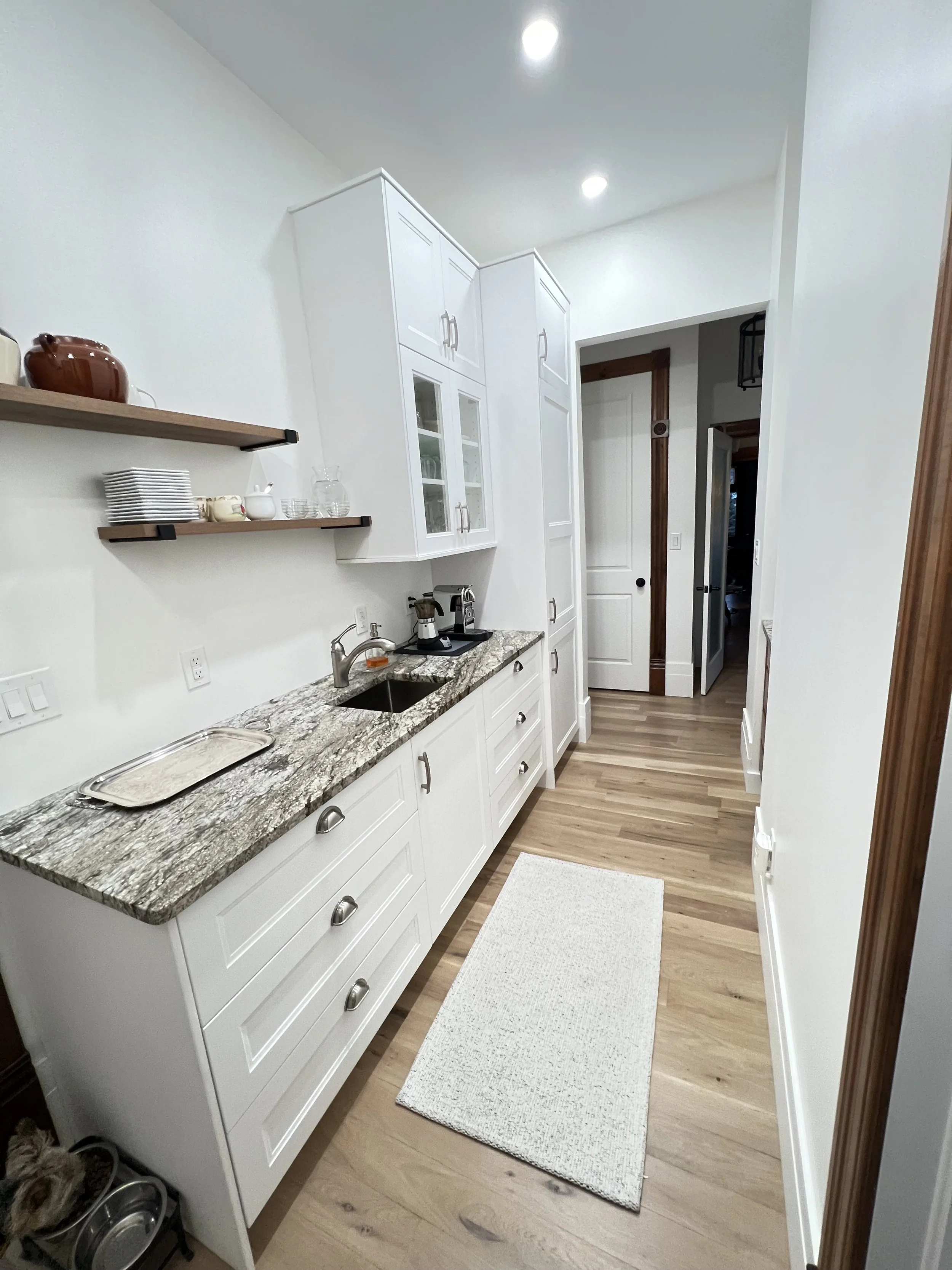 White cabinets, open wood shelves and a prep sink make practical use of this narrow pantry space.