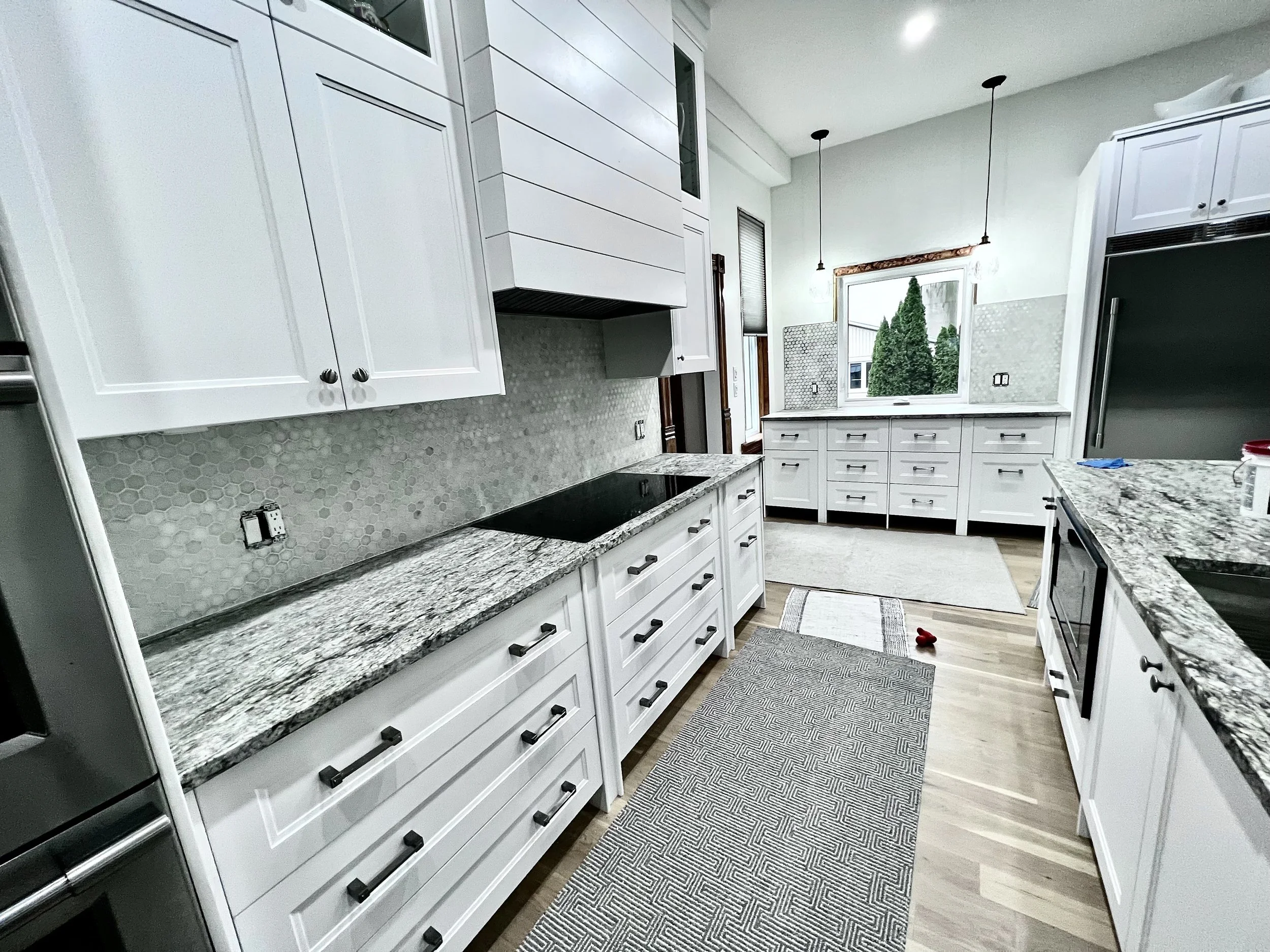 White drawers and cabinets frame the cooktop, with patterned counters and a hexagon tile backsplash adding texture.
