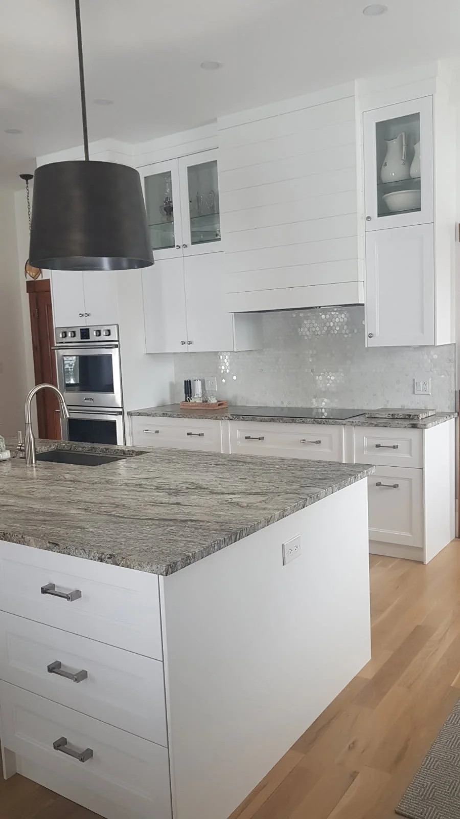 A shiplap-style range hood and glass-front cabinets carry the white finish up the wall, with extra drawer storage in the island.
