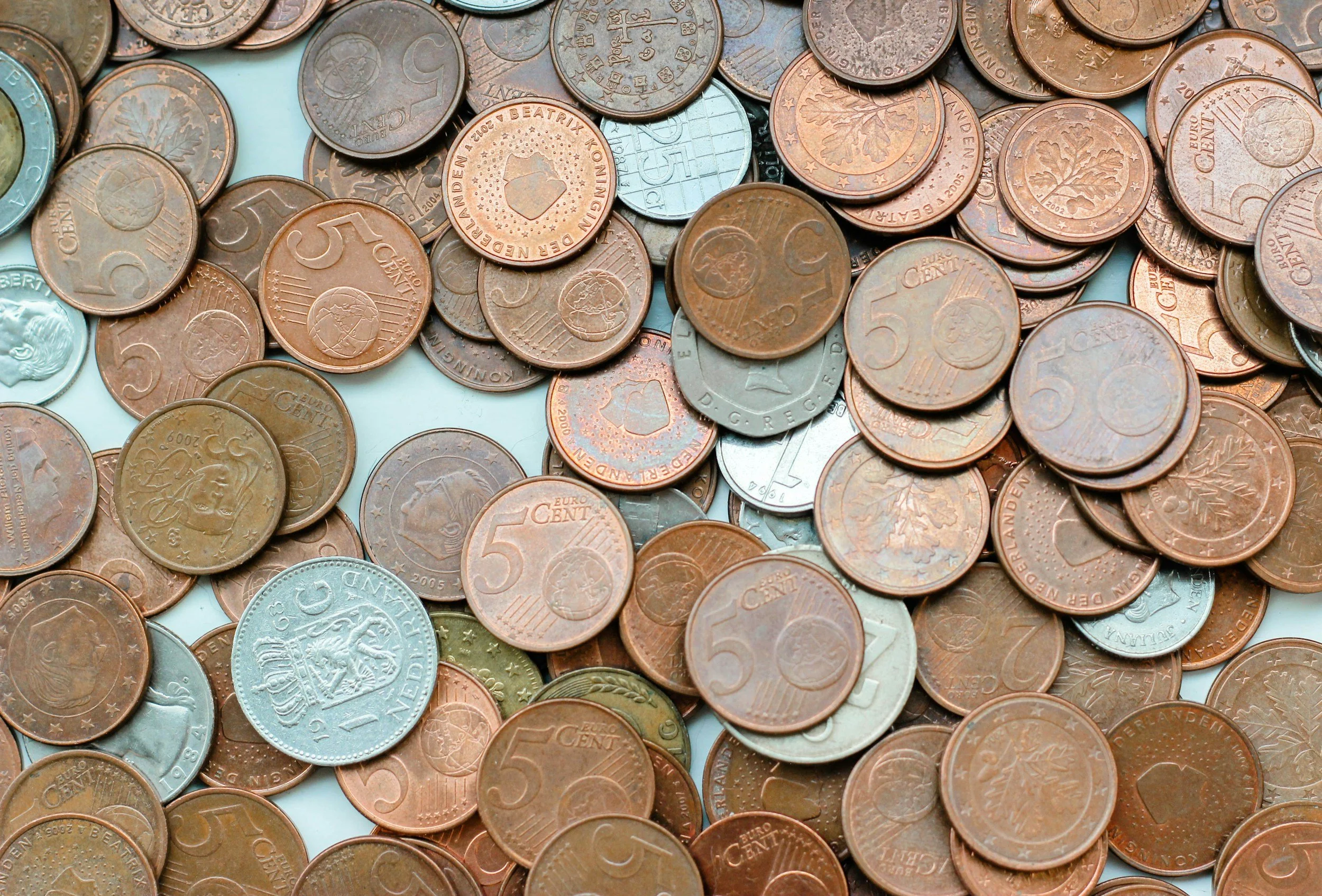 A close-up view of a collection of scattered Euro coins, mainly copper-colored 5-cent coins, with some 1-cent and 2-cent coins visible among them.