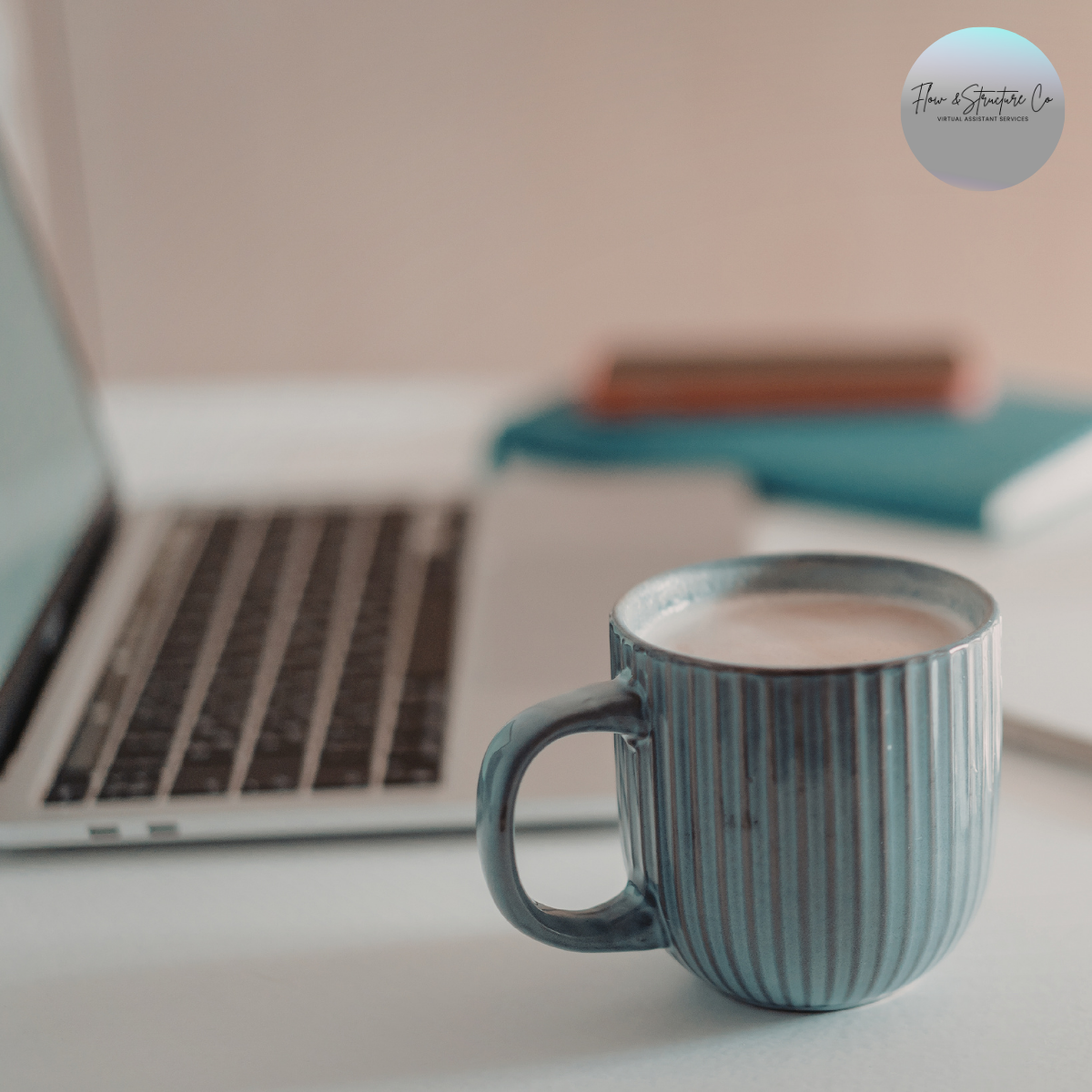 A striped ceramic mug filled with a hot beverage placed on a white desk, with a silver laptop and a closed blue and white notebook or planner in the background.