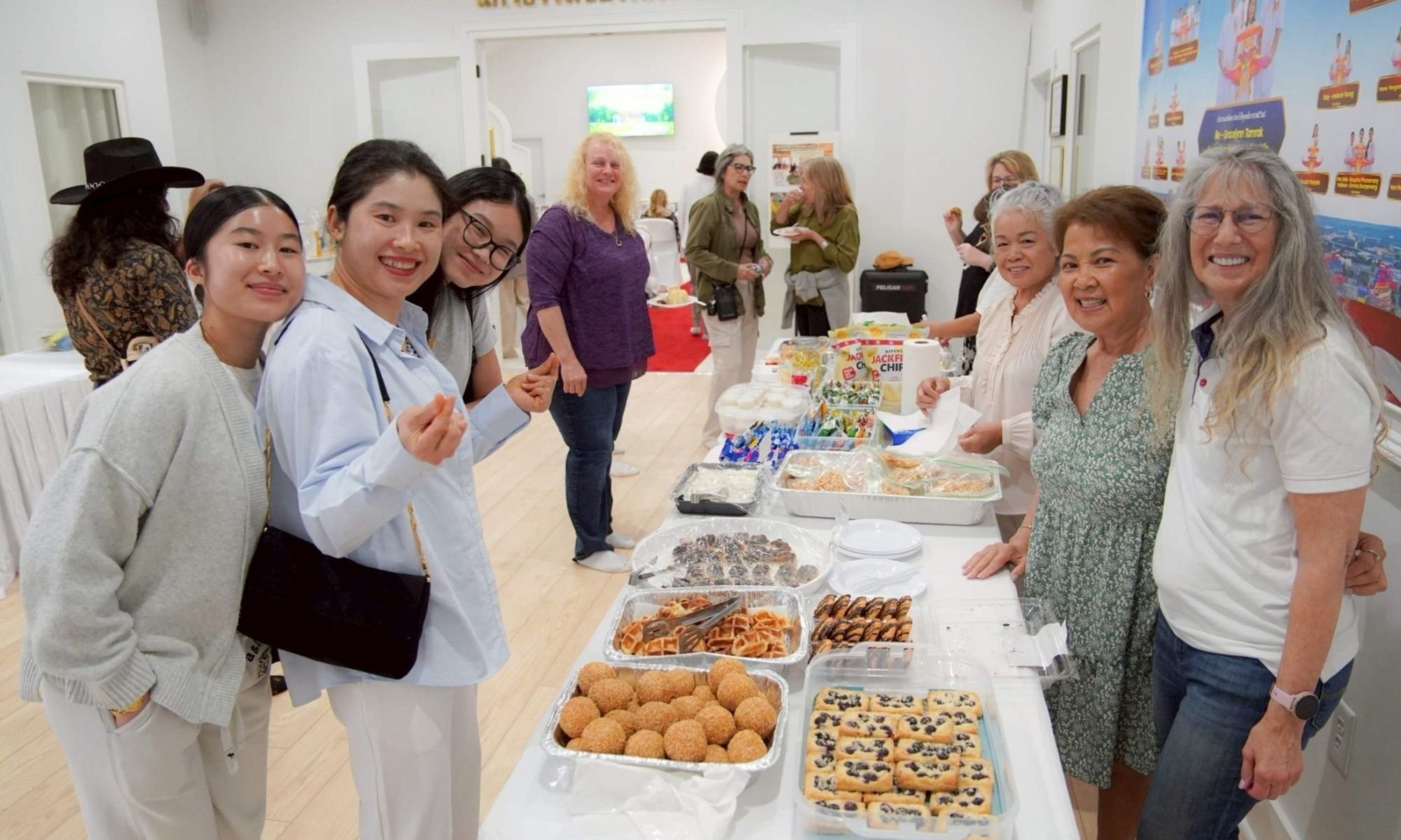 A group of women standing behind a table with various desserts at a community gathering or celebration.