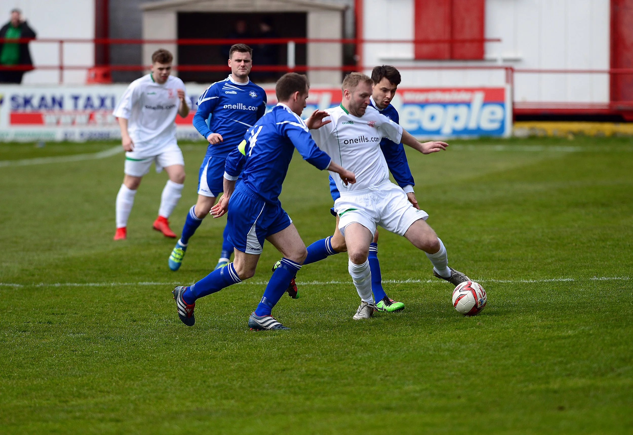 Soccer players in blue and white uniforms competing for the ball on a grassy field during a game.