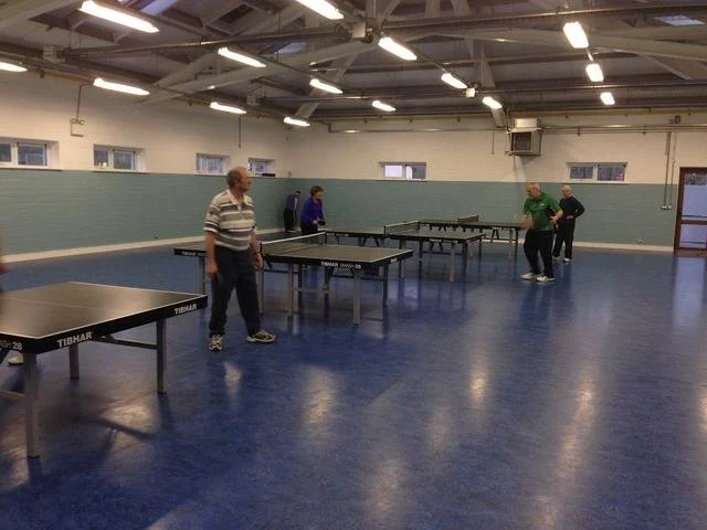 People playing table tennis in an indoor gym.