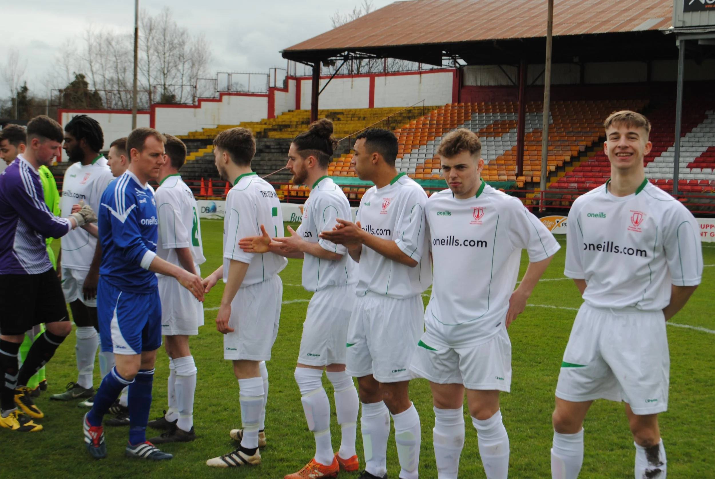 Soccer players standing in line before a match on a soccer field, with some players shaking hands.