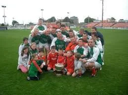 Group of young soccer players and coaches posing on a soccer field with a trophy.