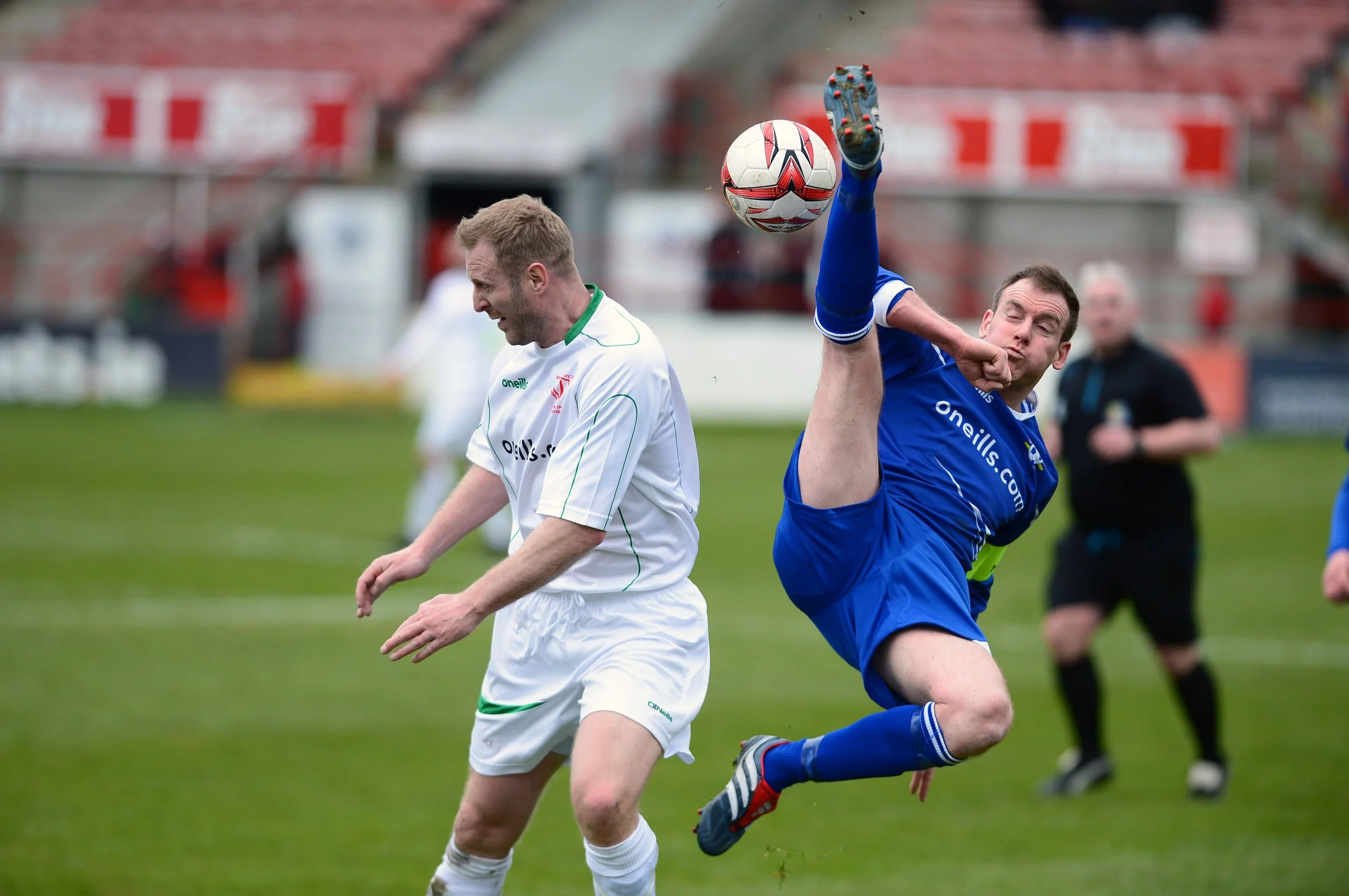 Two soccer players, one in a white uniform and the other in a blue uniform, competing for control of a soccer ball on the field during a match.