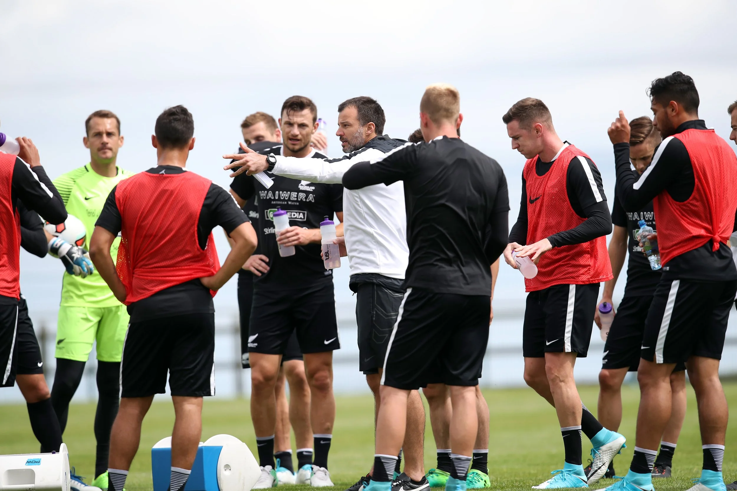 Soccer coach giving instructions to a team of players during practice on a grassy field.