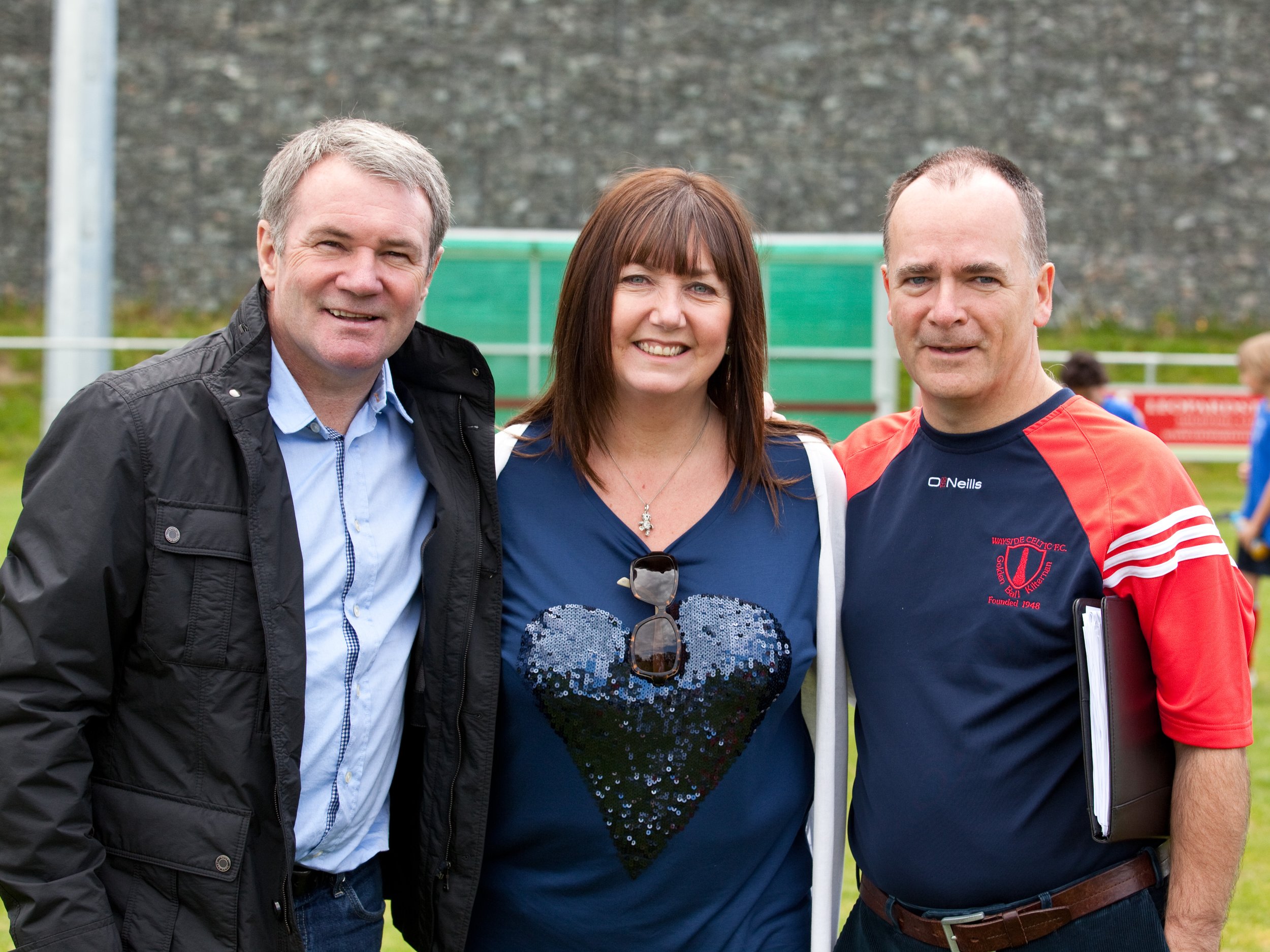 Three people standing outside on a sports field, smiling and posing for a photo.