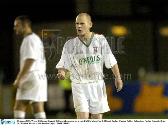 A soccer player with a shaved head wearing a white O'Neills soccer uniform on the field during a game.