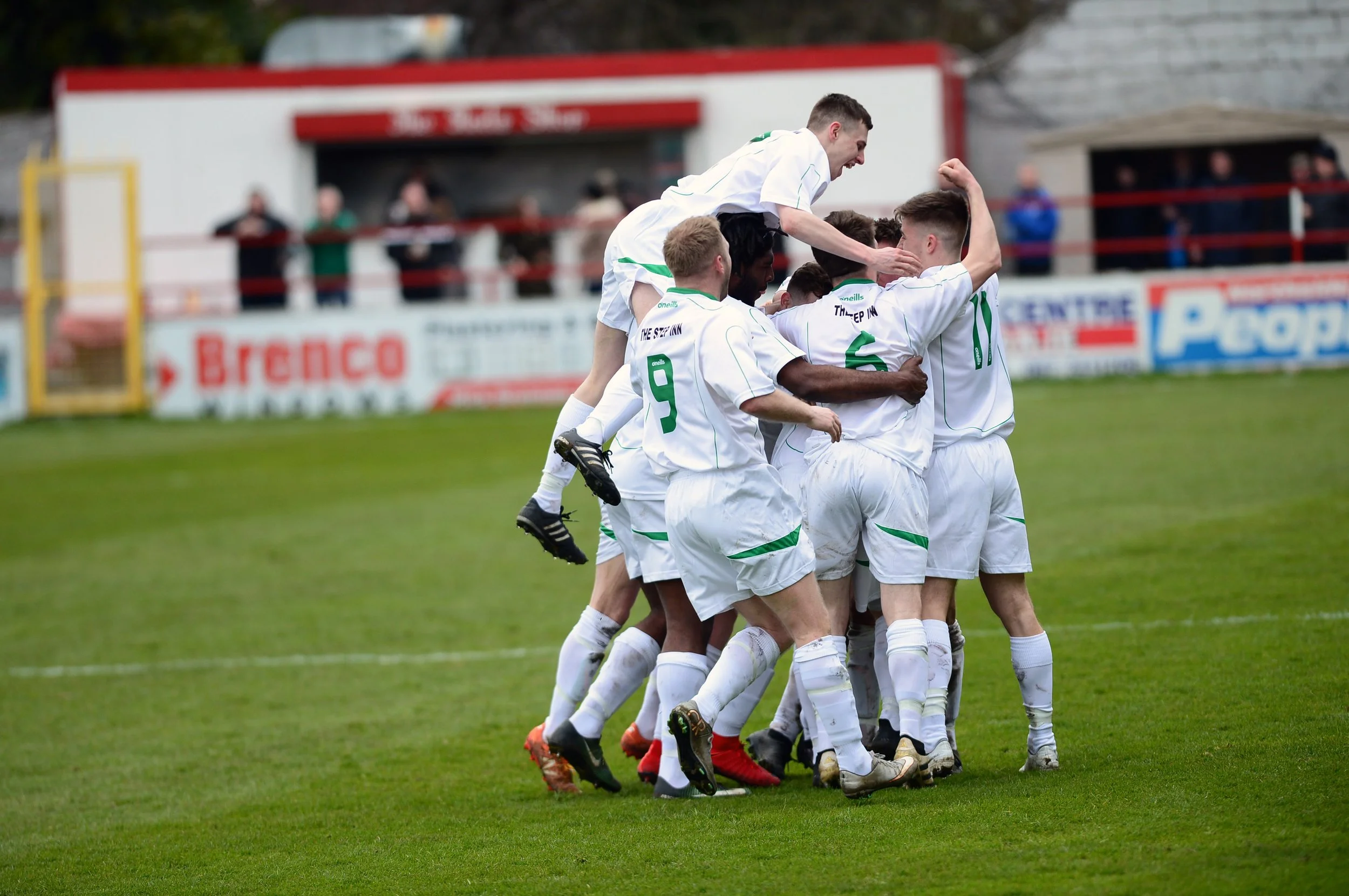 A group of soccer players in white uniforms celebrates together on the field, with some jumping and others hugging.