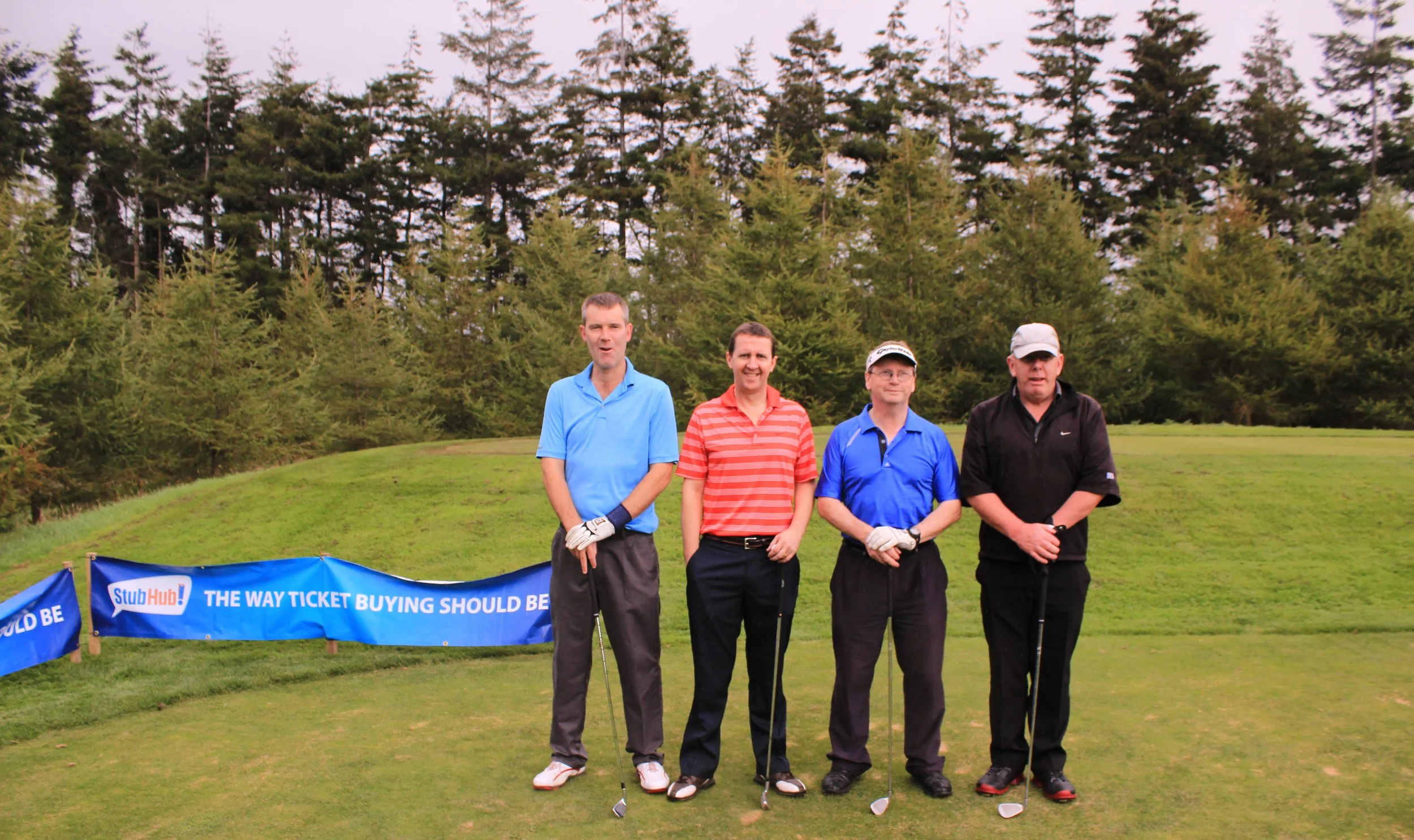 Four men standing on a golf course in front of a banner that reads "StubHub! THE WAY TICKET BUYING SHOULD BE" with trees in the background.