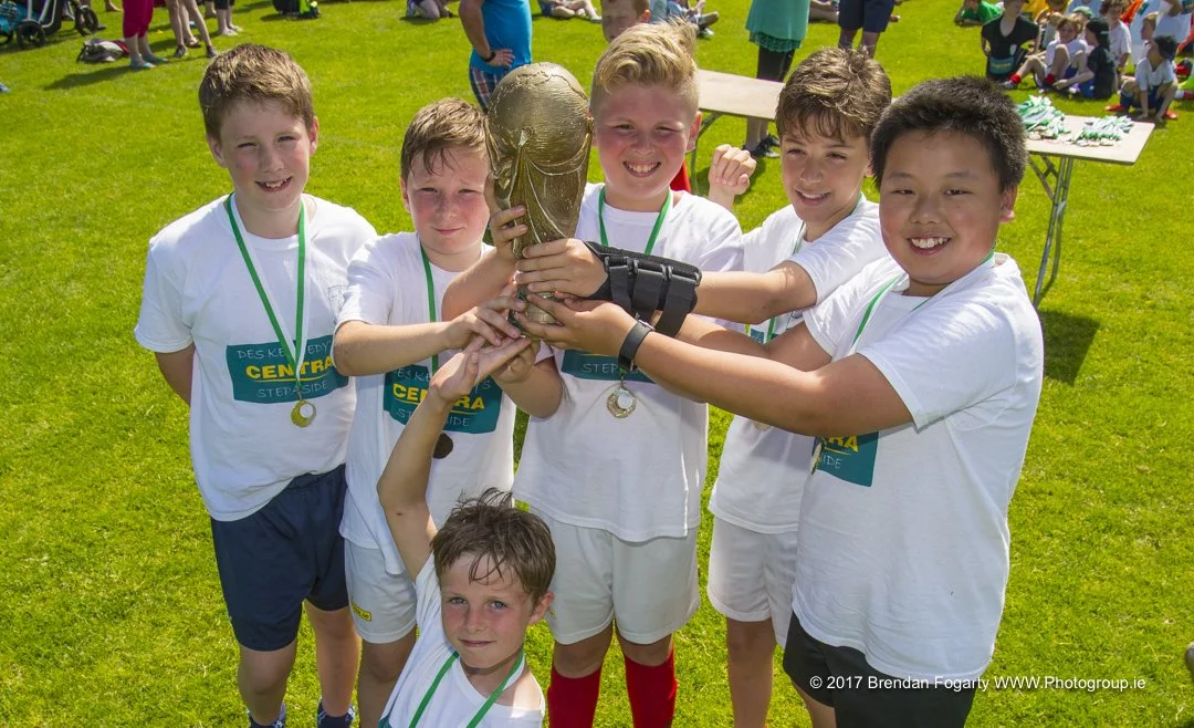 Group of young boys celebrating with a trophy after a sports game on a grassy field.